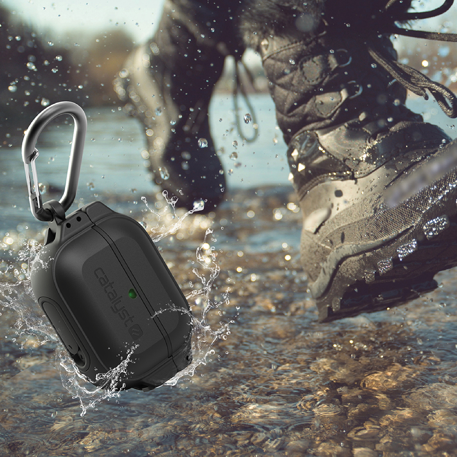 Schwarze AirPods-Hülle mit Karabiner im Wasser, im Hintergrund tritt eine Person mit Stiefeln durch das Wasser.