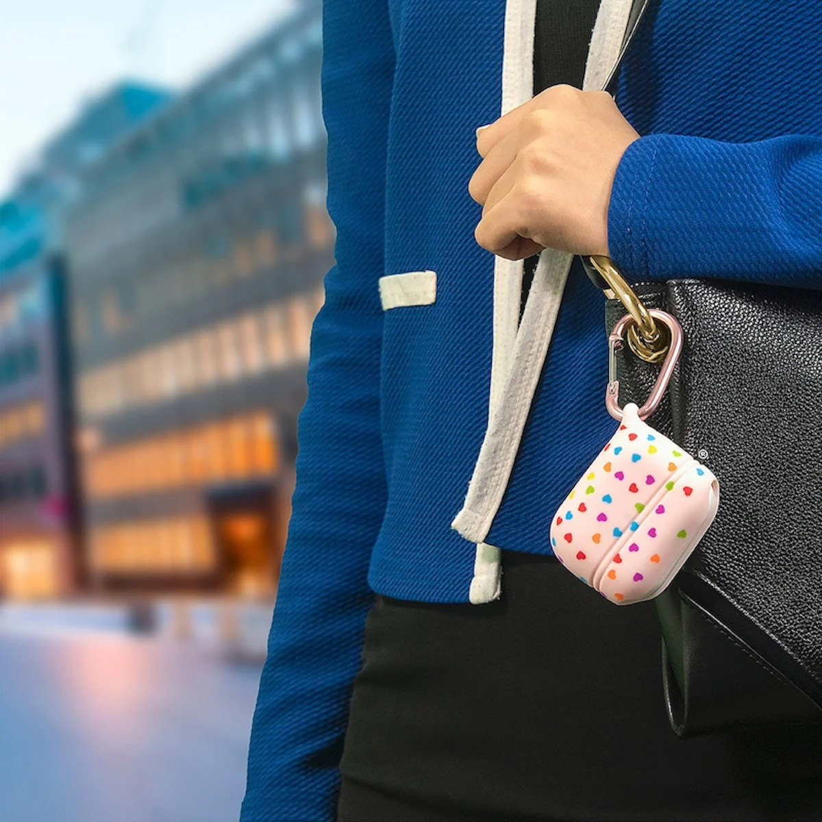 Eine Person in einer blauen Jacke hält eine schwarze Handtasche mit einer pinken AirPods-Hülle.