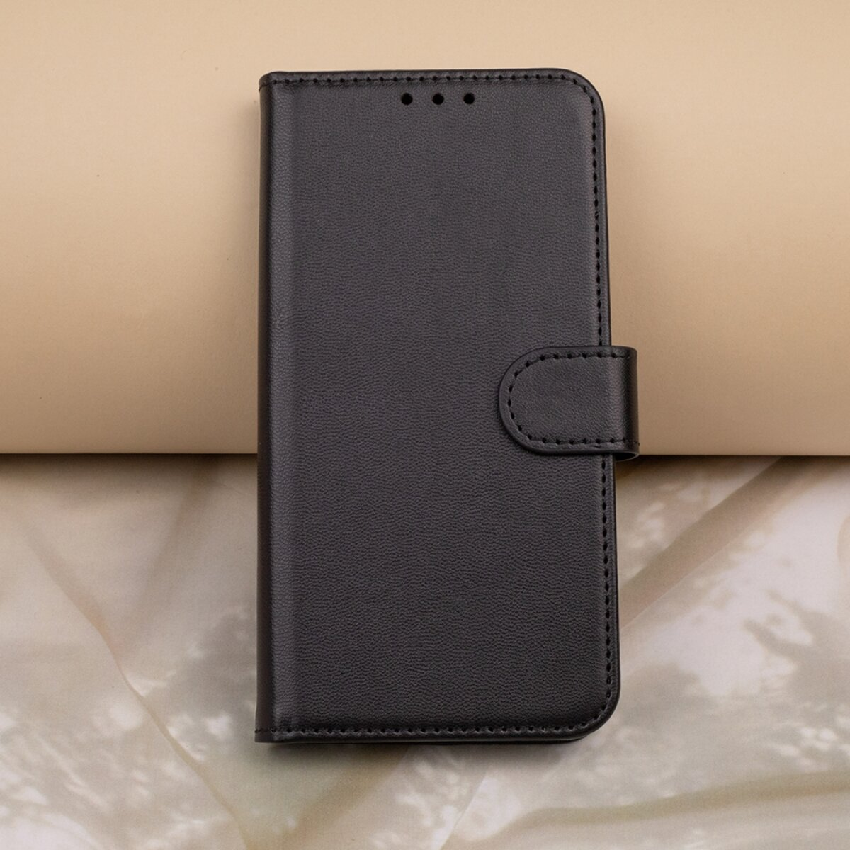 Eine geschlossene schwarze Ledertasche für Smartphones mit Magnetverschlusslasche auf beige-weißem Hintergrund.