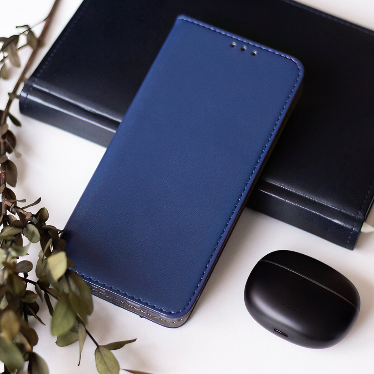 Blaue Smartphone-Hülle, schwarzer Notizblock und Ohrhörer auf weißem Tisch.