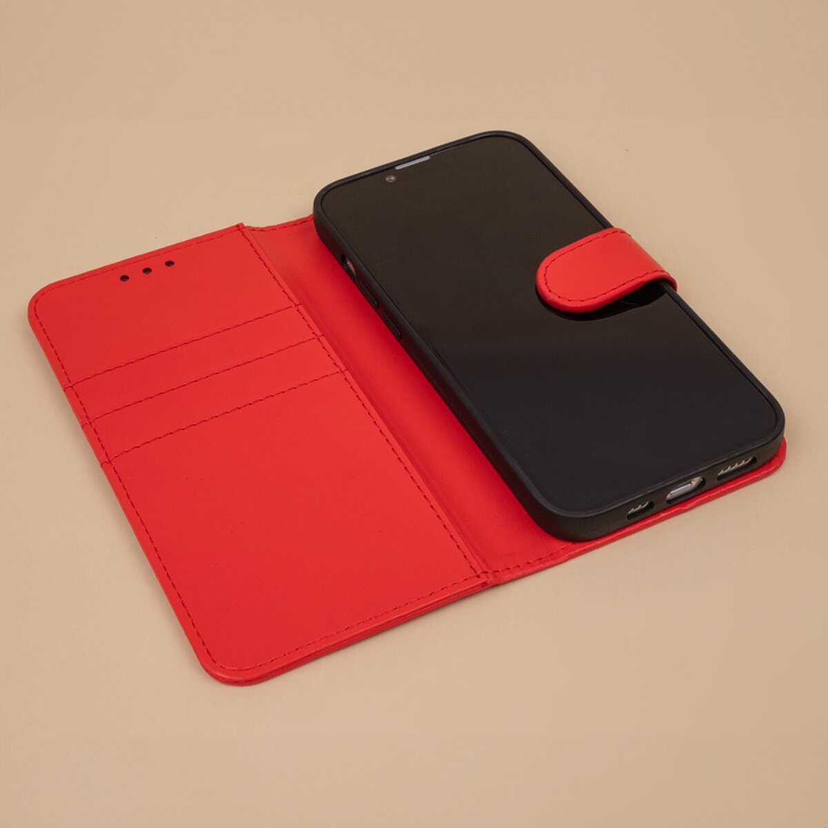 Ein schwarzes Smartphone in einer roten Lederhülle mit Kartenfächern auf einem beigen Hintergrund.