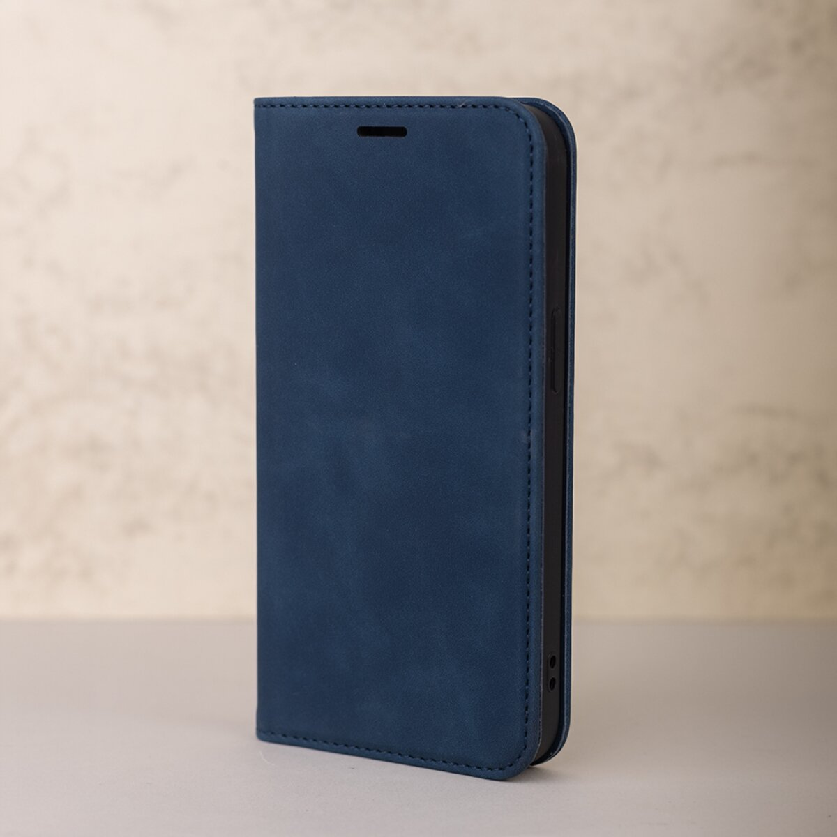 Eine geschlossene blaue Smartphone-Ledertasche steht aufrecht auf einer grauen Oberfläche vor verschwommenem Hintergrund.