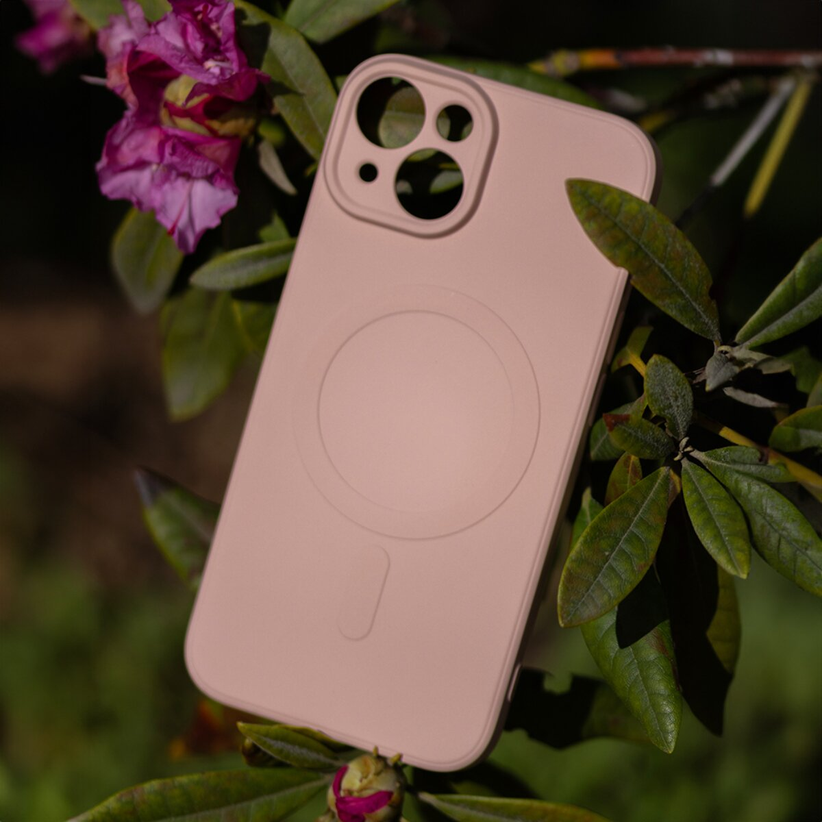 Eine rosa Handyhülle mit MagSafe-Ring, eingebettet zwischen grünen Blättern und lila Blüten.
