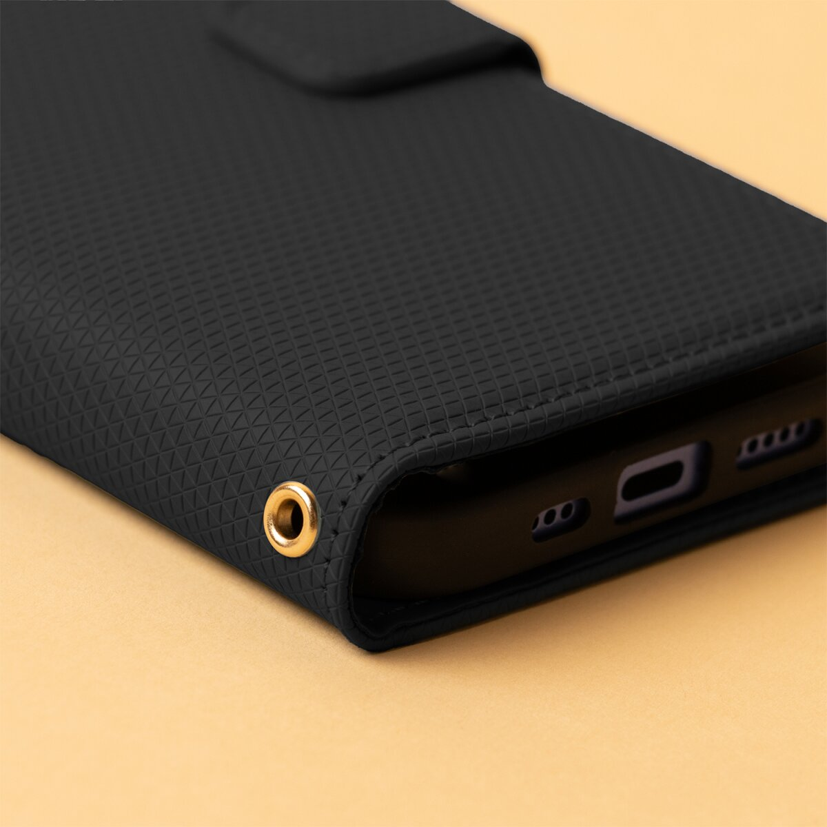 Eine schwarze Smartphone-Hülle mit strukturiertem Muster und goldener Öse auf beigem Hintergrund.