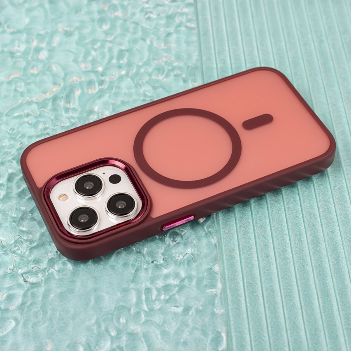 Eine bordeauxrote Smartphone-Hülle mit MagSafe-Ring auf einer strukturierten türkisfarbenen Oberfläche.