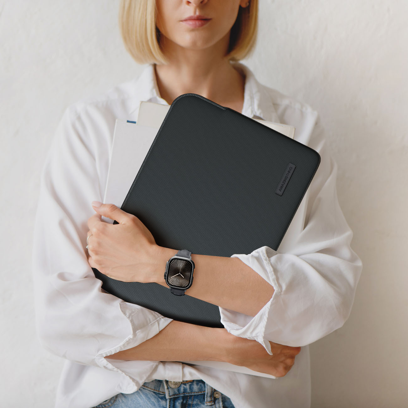 Una donna con camicia bianca tiene una custodia nera per laptop e documenti. Indossa un orologio.