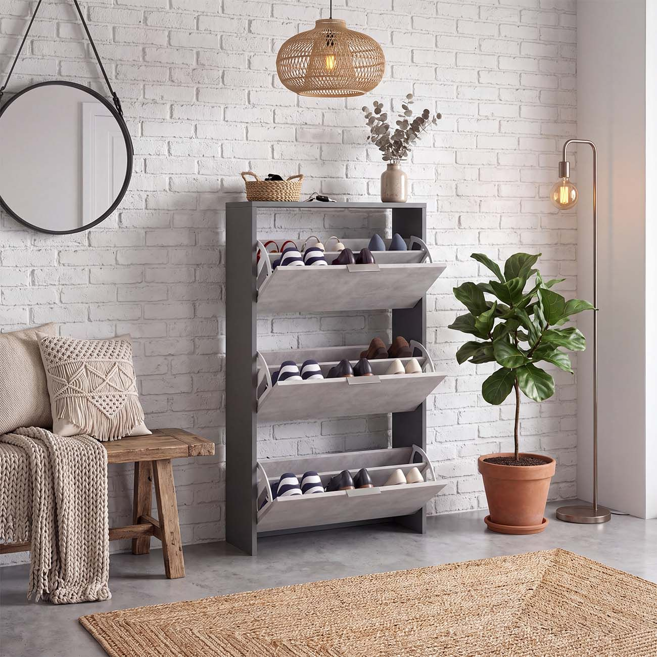 Pasillo luminoso con zapatero gris, pared de ladrillo blanco, espejo colgante, banco de madera y planta.