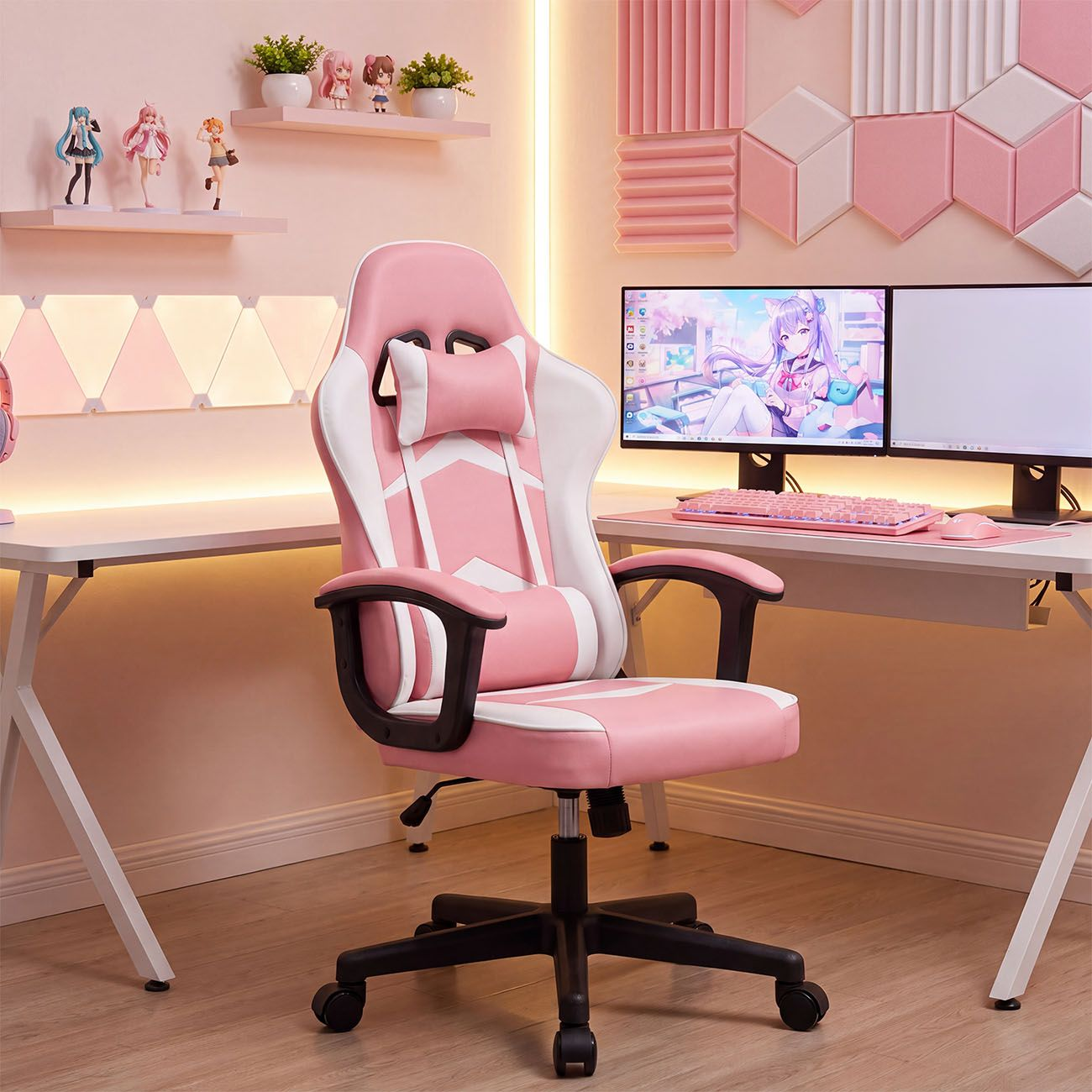 Una silla gamer rosa y blanca en una habitación rosa con dos monitores y figuras de anime.