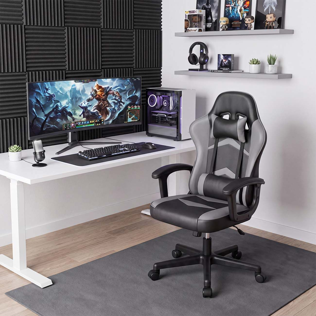Configuración de juego con escritorio blanco, monitor ultra ancho, torre de PC y silla ergonómica gris y negra.