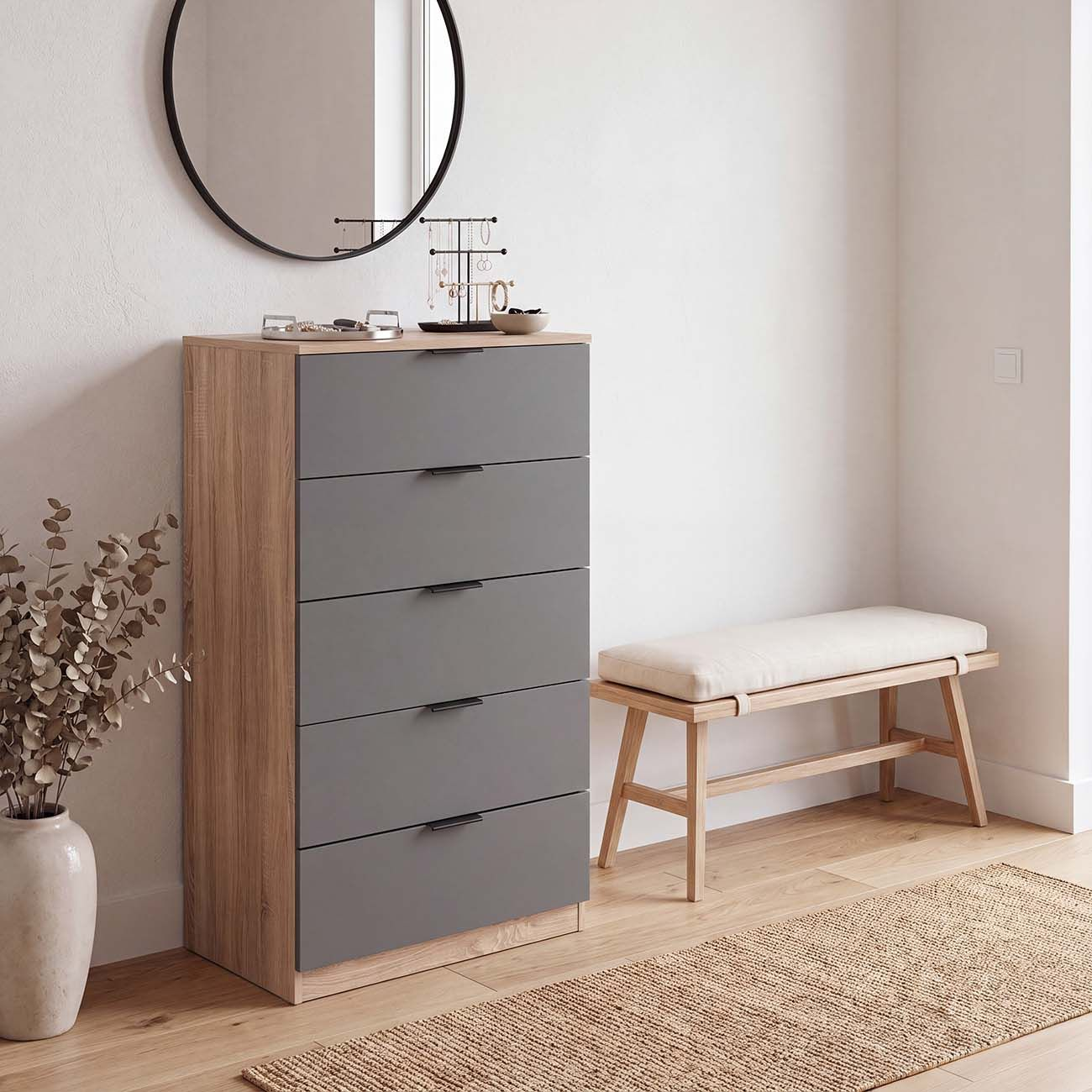 Cómoda de madera con cajones grises, espejo redondo, joyero, banco y un jarrón con flores secas.