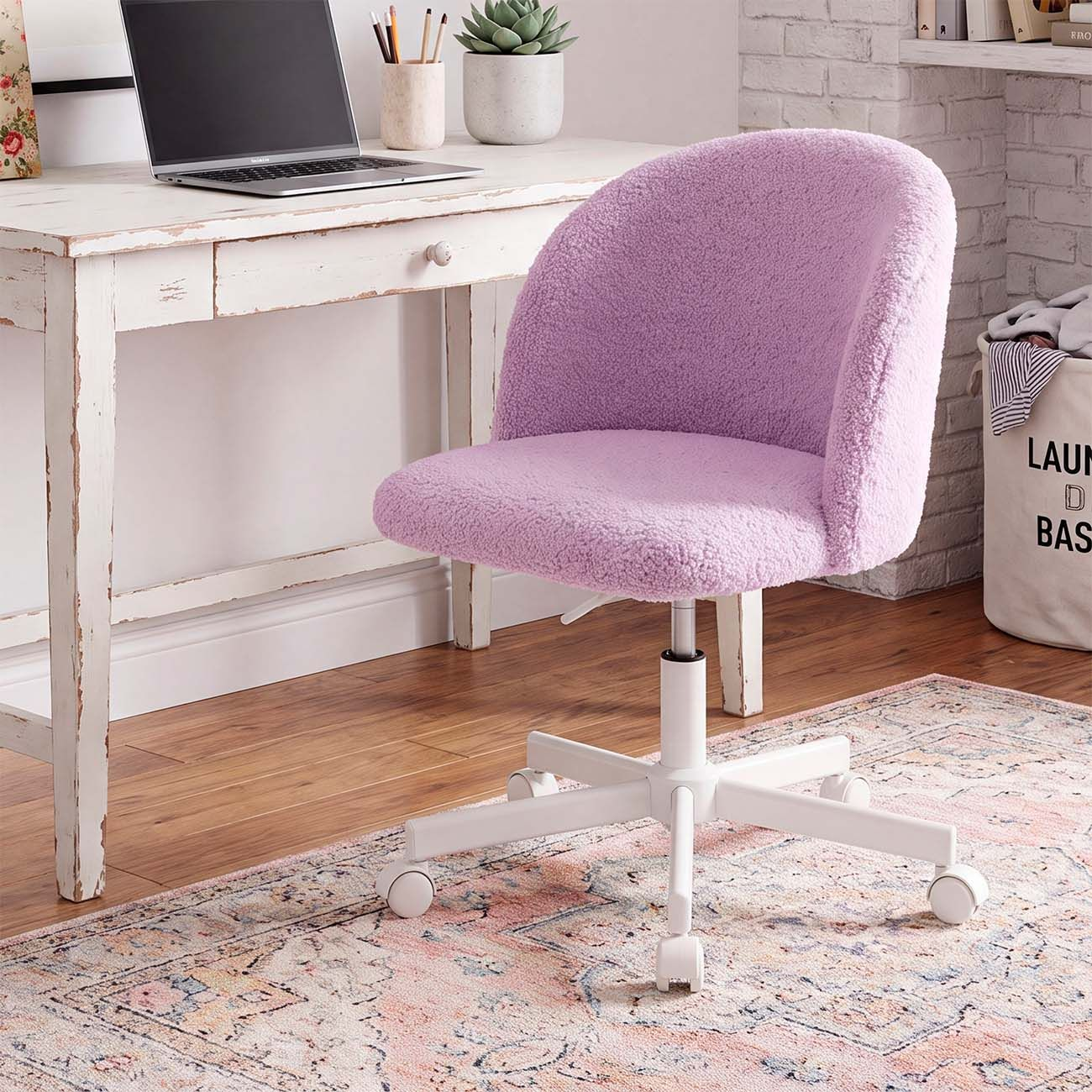 Una silla de oficina de felpa lila está frente a un escritorio blanco sobre una alfombra estampada.