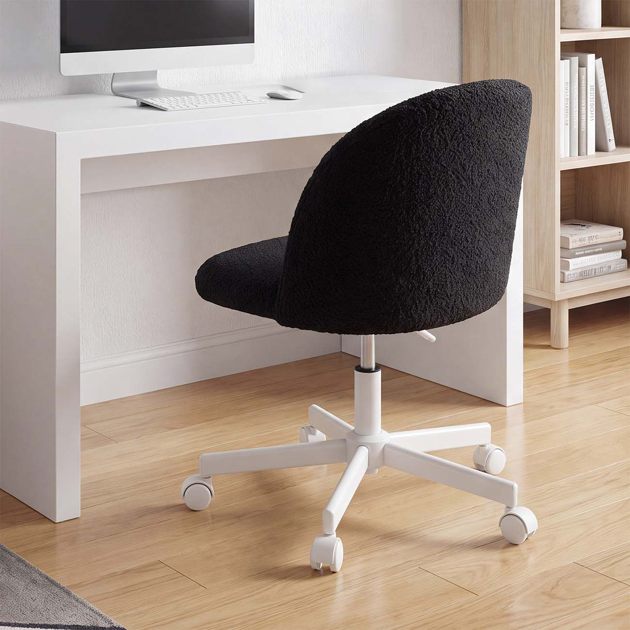 Una silla de oficina negra con base blanca está frente a un escritorio blanco en suelo de madera.
