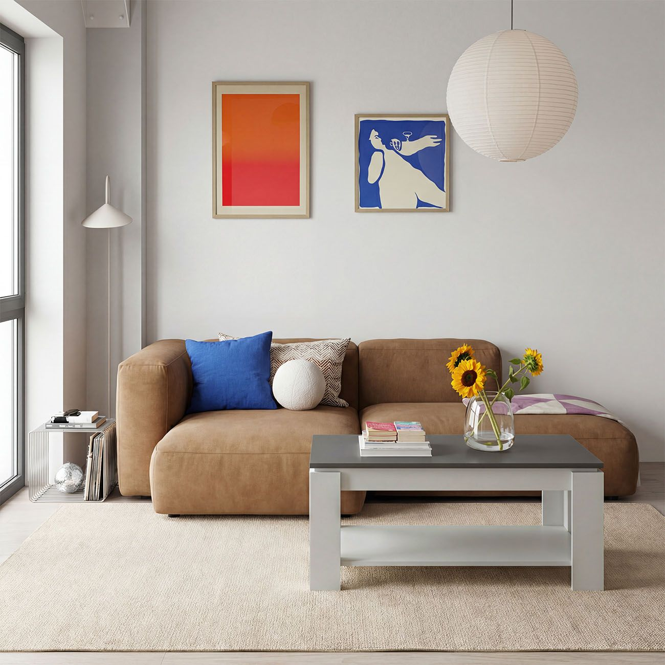 Una sala de estar acogedora con sofá marrón, mesa de centro blanca con girasoles, cuadros coloridos y lámpara colgante.