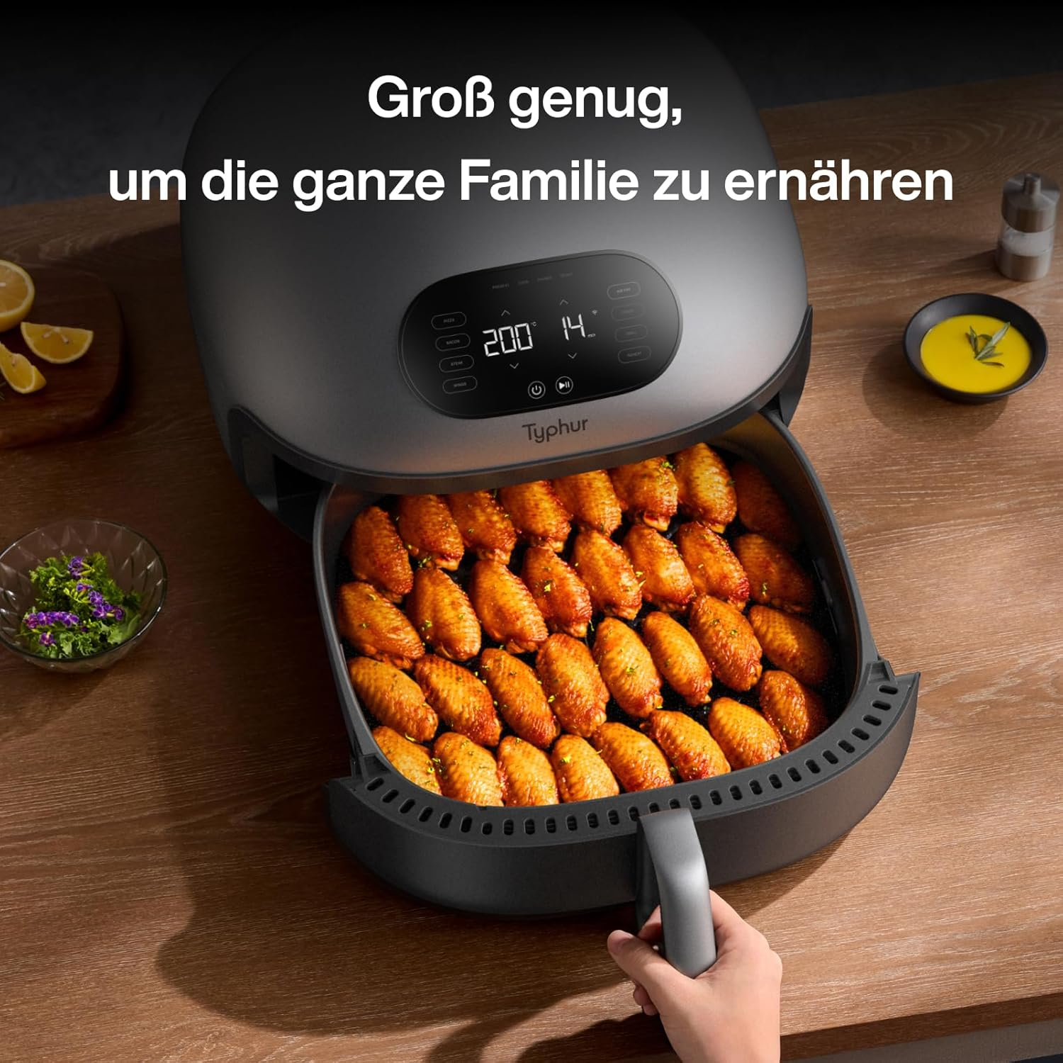 Eine Hand zieht die Schublade einer großen grauen Heißluftfritteuse auf, gefüllt mit knusprigen Hähnchenflügeln.