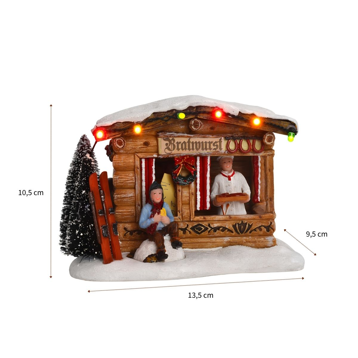 A snowy Christmas bratwurst chalet figurine with figures, skis, a tree, and colored lights.