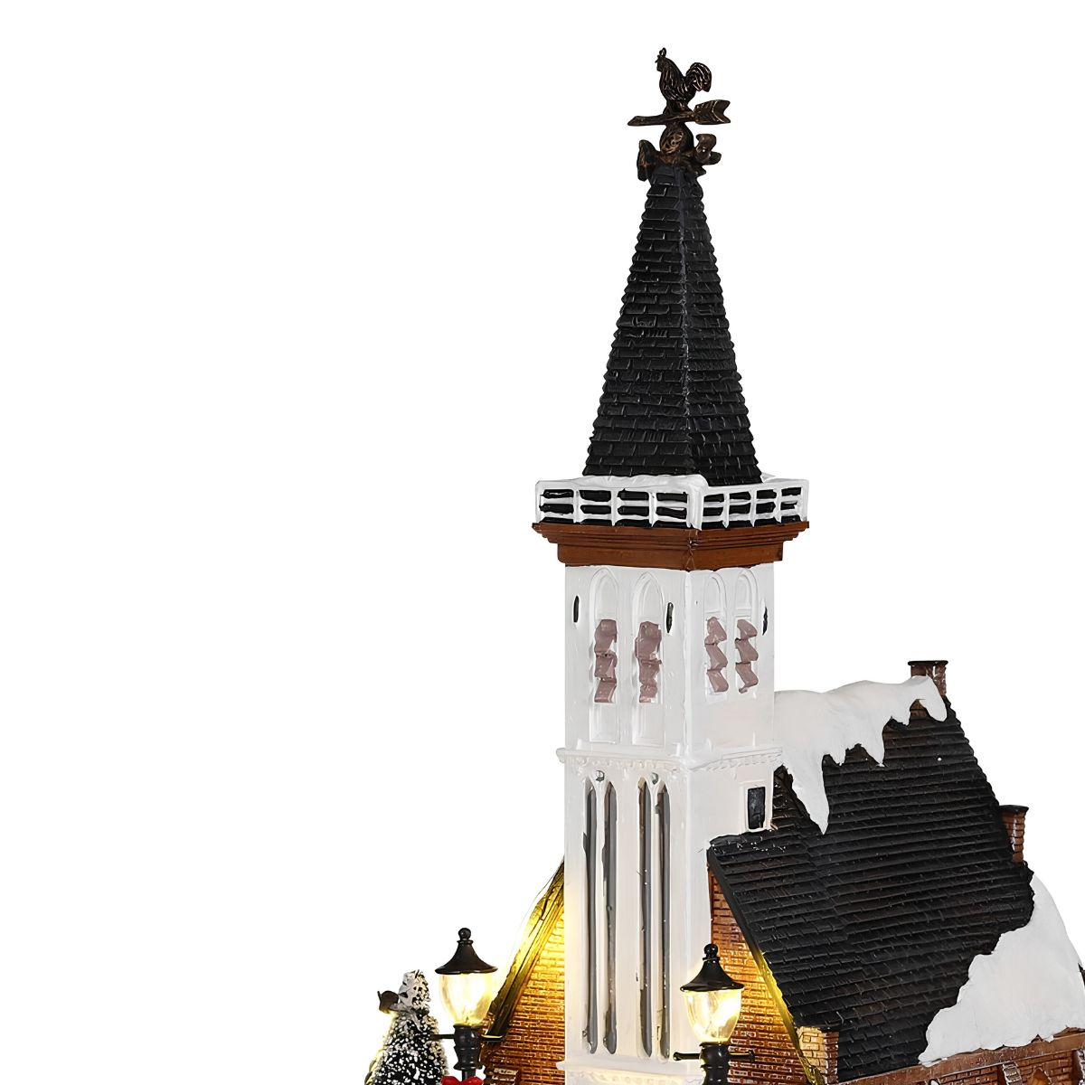 Model of a snow-covered church with a steeple, weather vane, and lit lanterns.