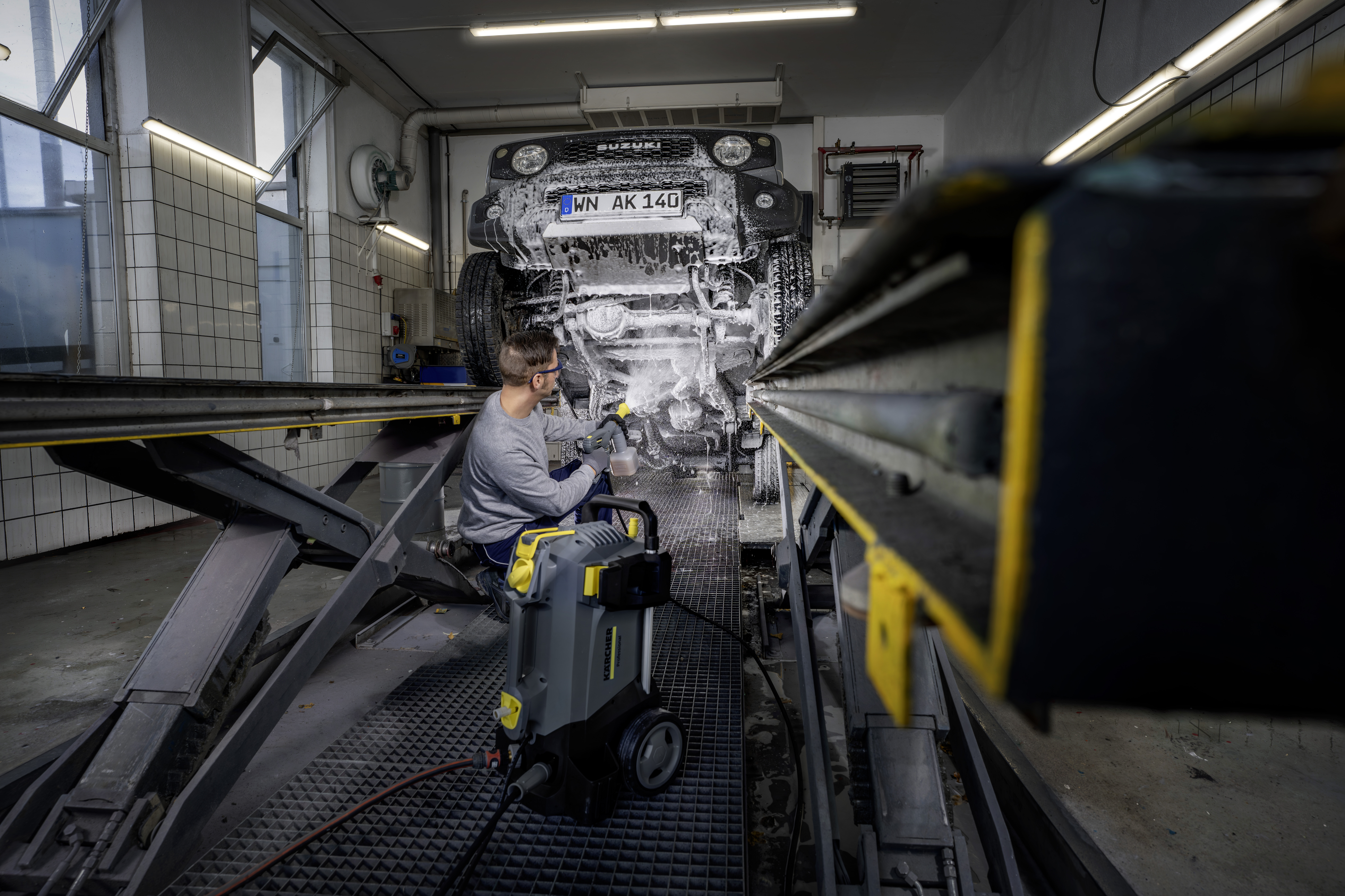 Ein Arbeiter wäscht das Unterteil eines Autos mit einem Hochdruckreiniger in einer Werkstatt.