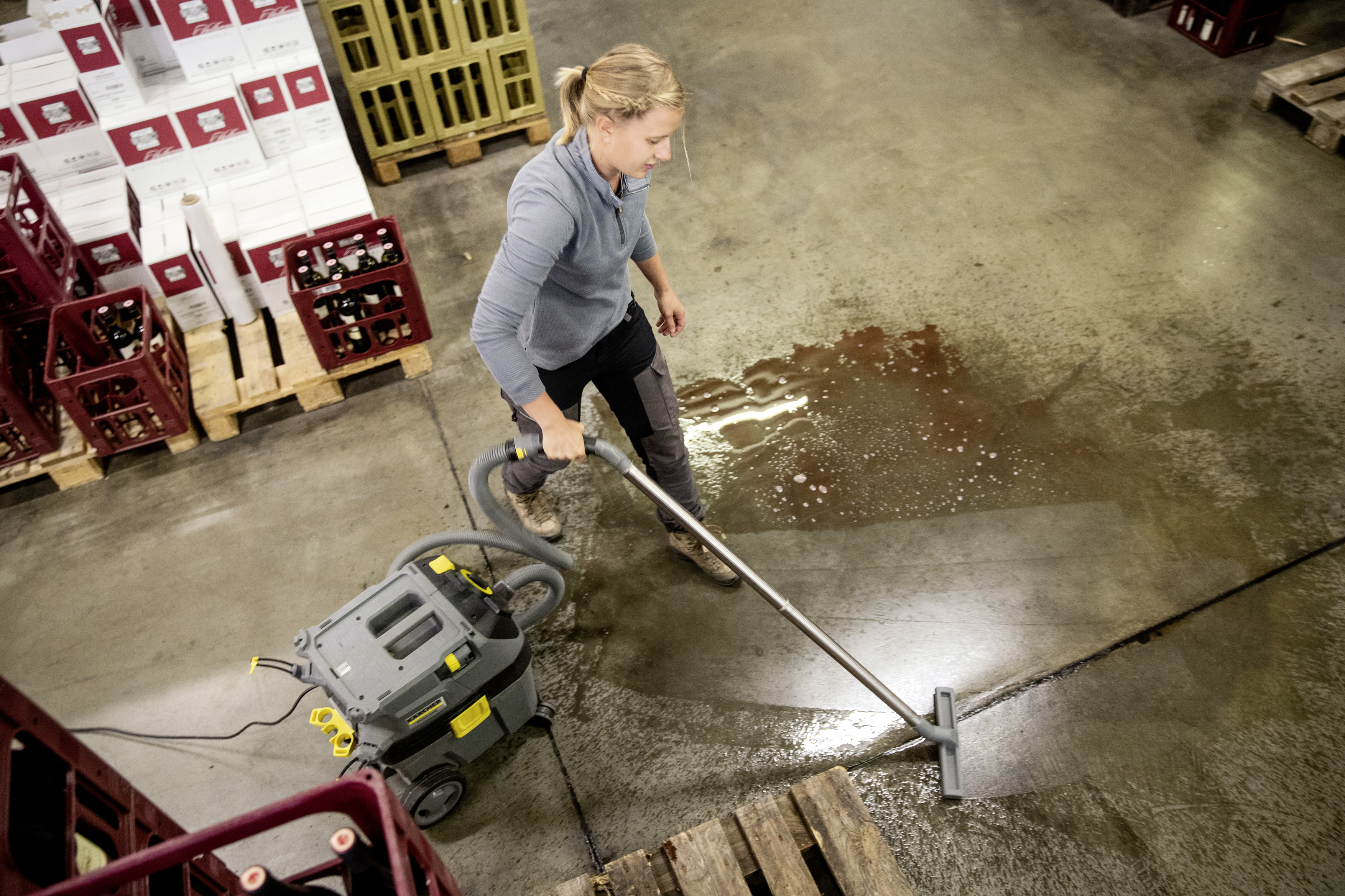 Una donna usa un aspiratore per liquidi per pulire un pavimento di cemento bagnato.