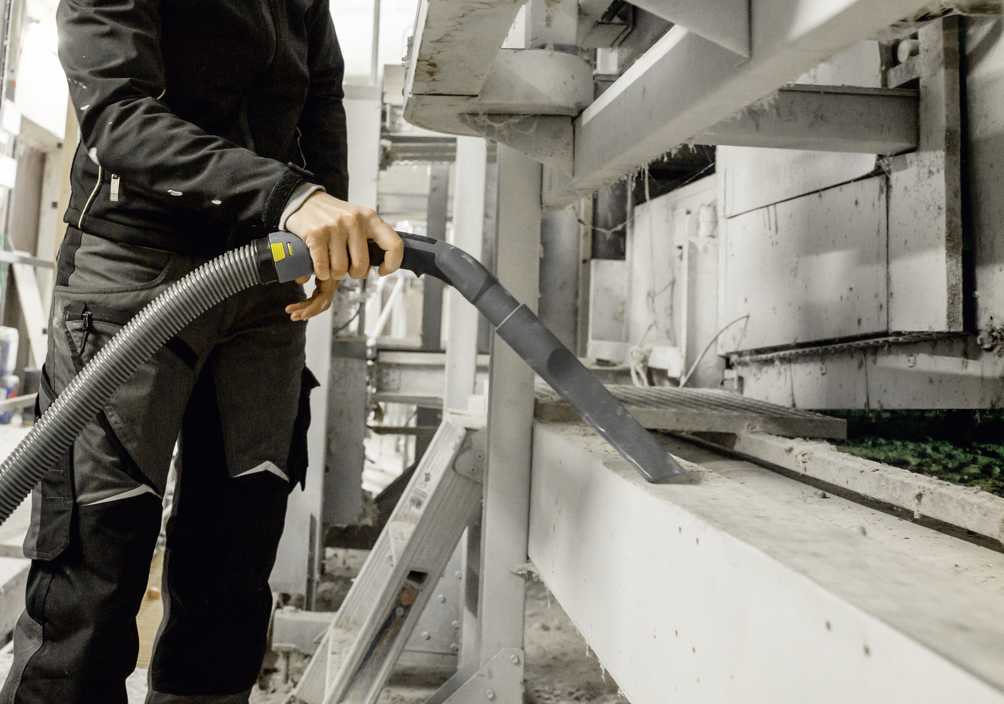 Un lavoratore con abiti scuri aspira la polvere dai macchinari industriali in una fabbrica.