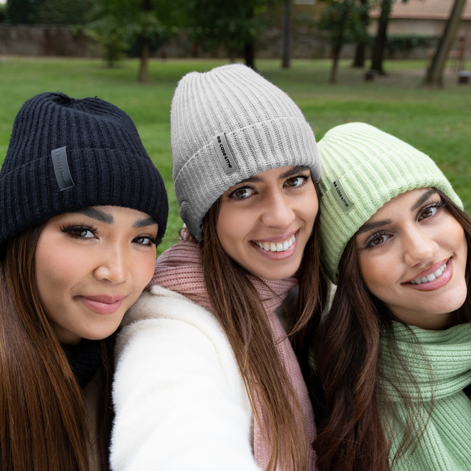 Tres mujeres sonrientes con gorros coloridos se hacen un selfi en un parque.