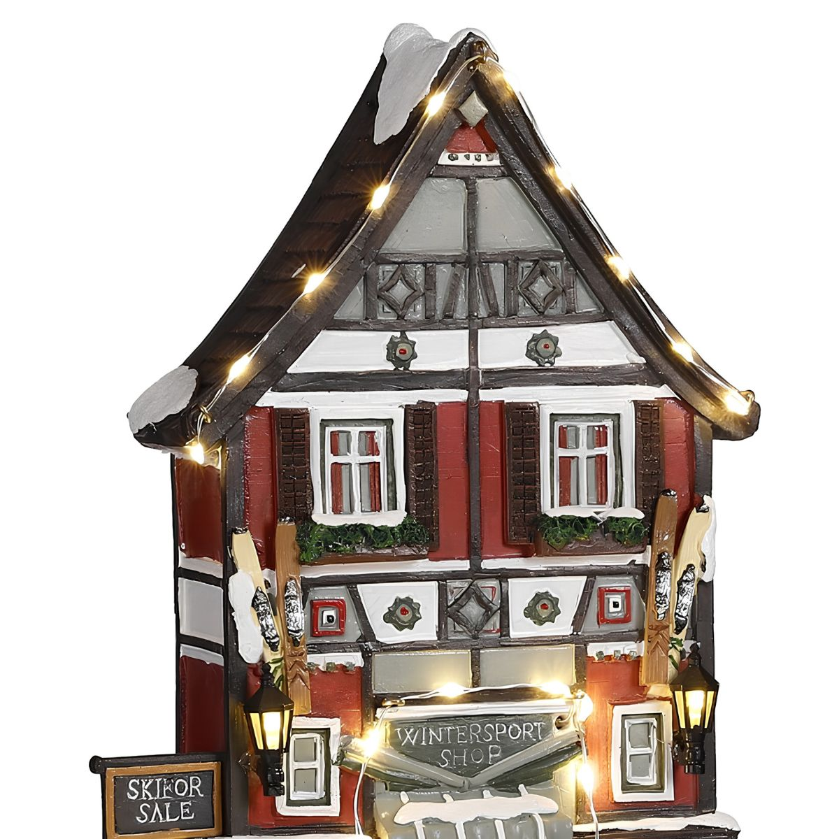 Un chalet miniature enneigé en magasin de sports d'hiver, décoré de guirlandes lumineuses.