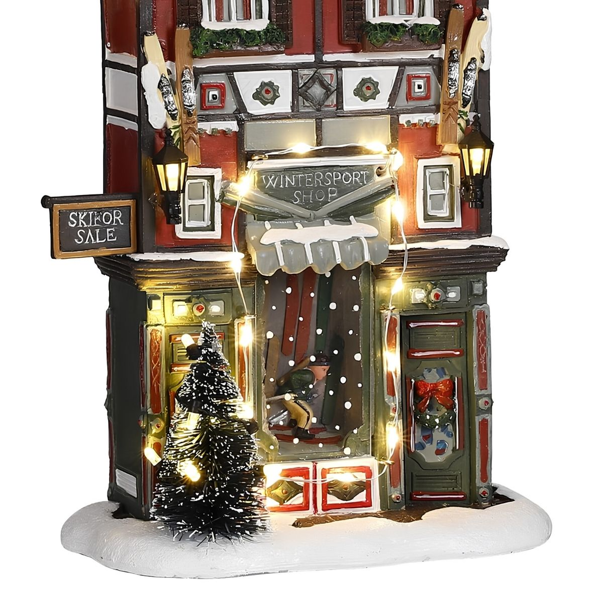 Bâtiment de sports d'hiver illuminé avec des skis et un arbre miniature dans la neige.