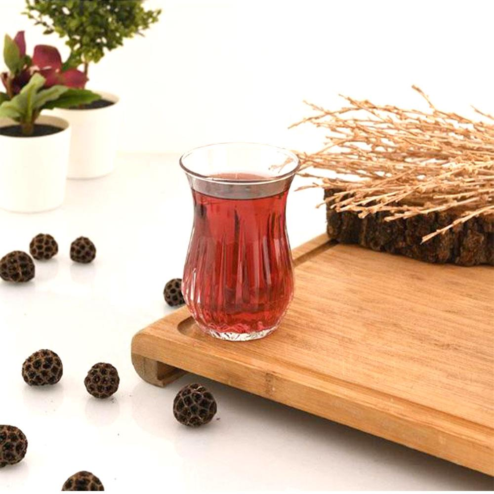 Ahşap bir tepsi üzerinde kırmızı çay bardağı, dekoratif tohumlar ve dallar.