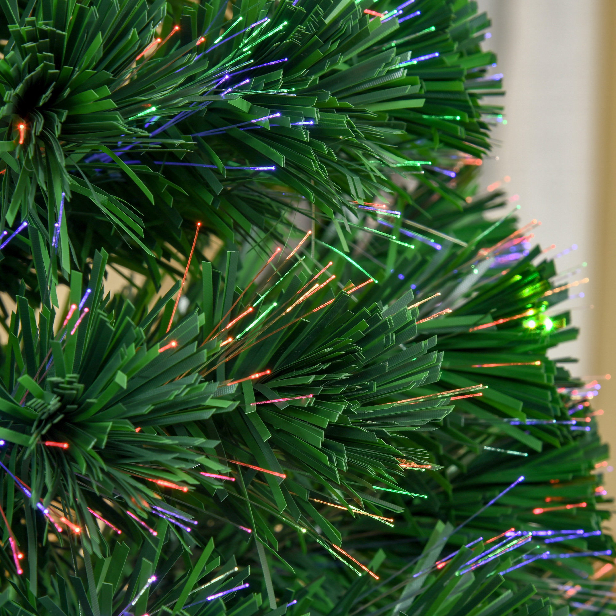 Primer plano de un árbol de Navidad artificial con agujas verdes y luces de fibra óptica brillantes.