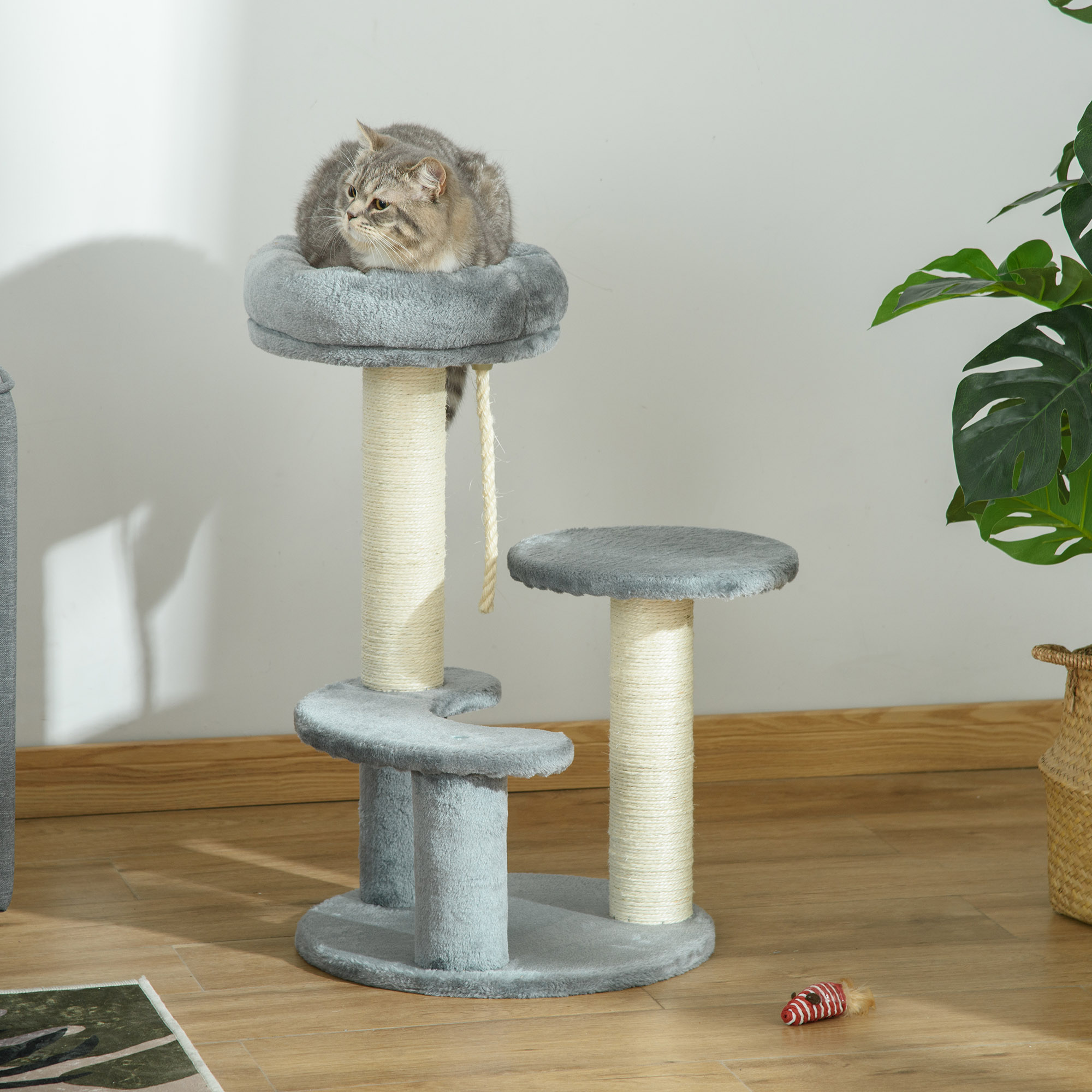 Un gato gris yace en la cama superior de un árbol para gatos gris de varios niveles en el interior.