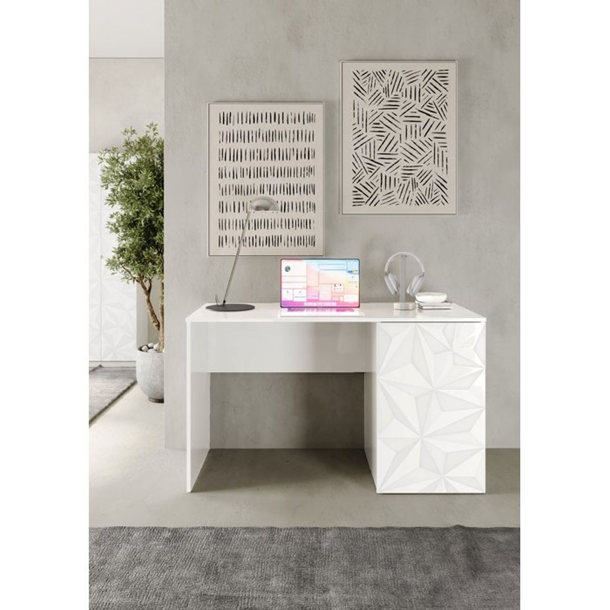 Ein weißer Schreibtisch mit offenem Laptop, Lampe und Kopfhörern vor grauer Wand mit abstrakter Kunst.