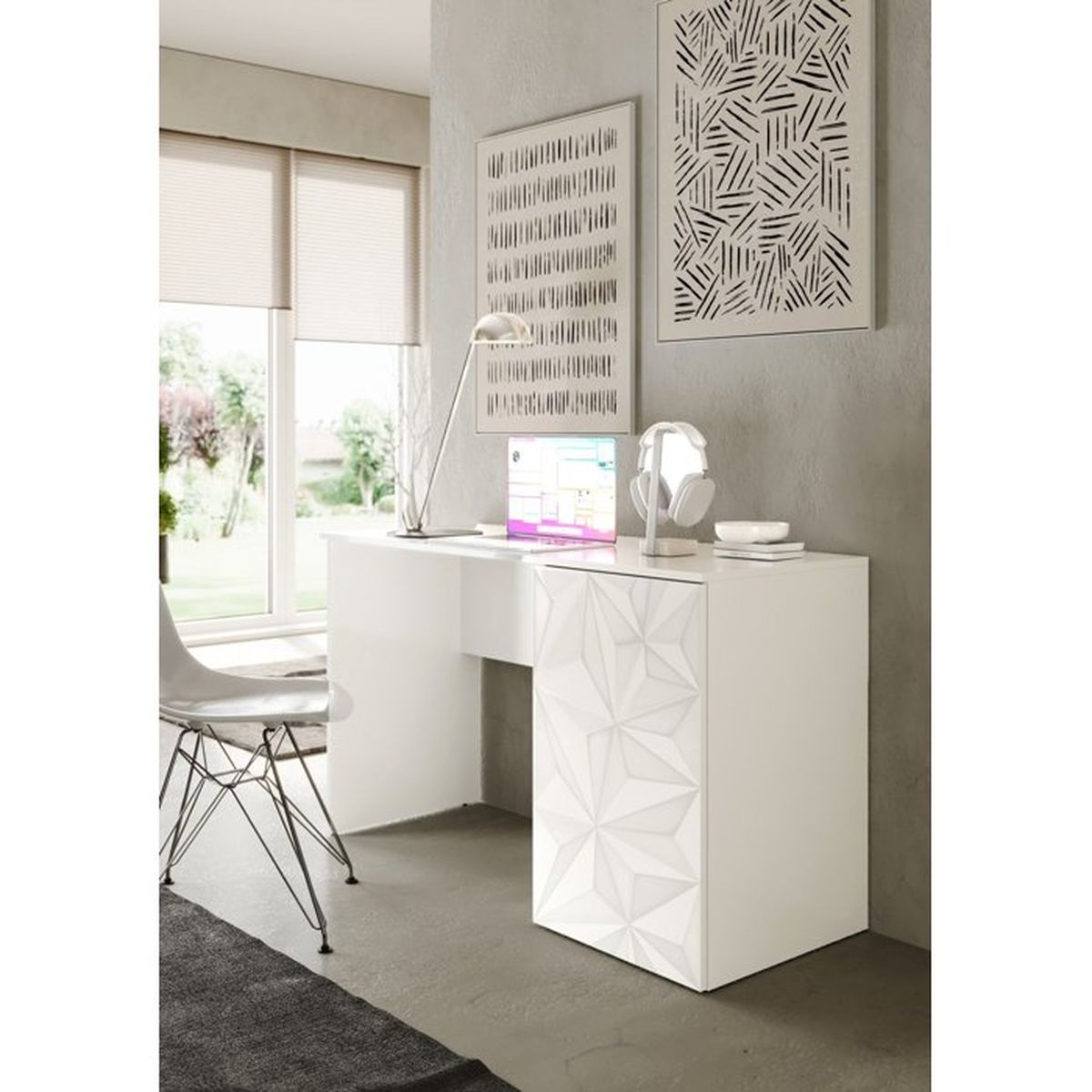 Ein weißer Schreibtisch mit geometrischem Frontdesign steht in einem hellen Raum vor einer grauen Wand mit Bildern.