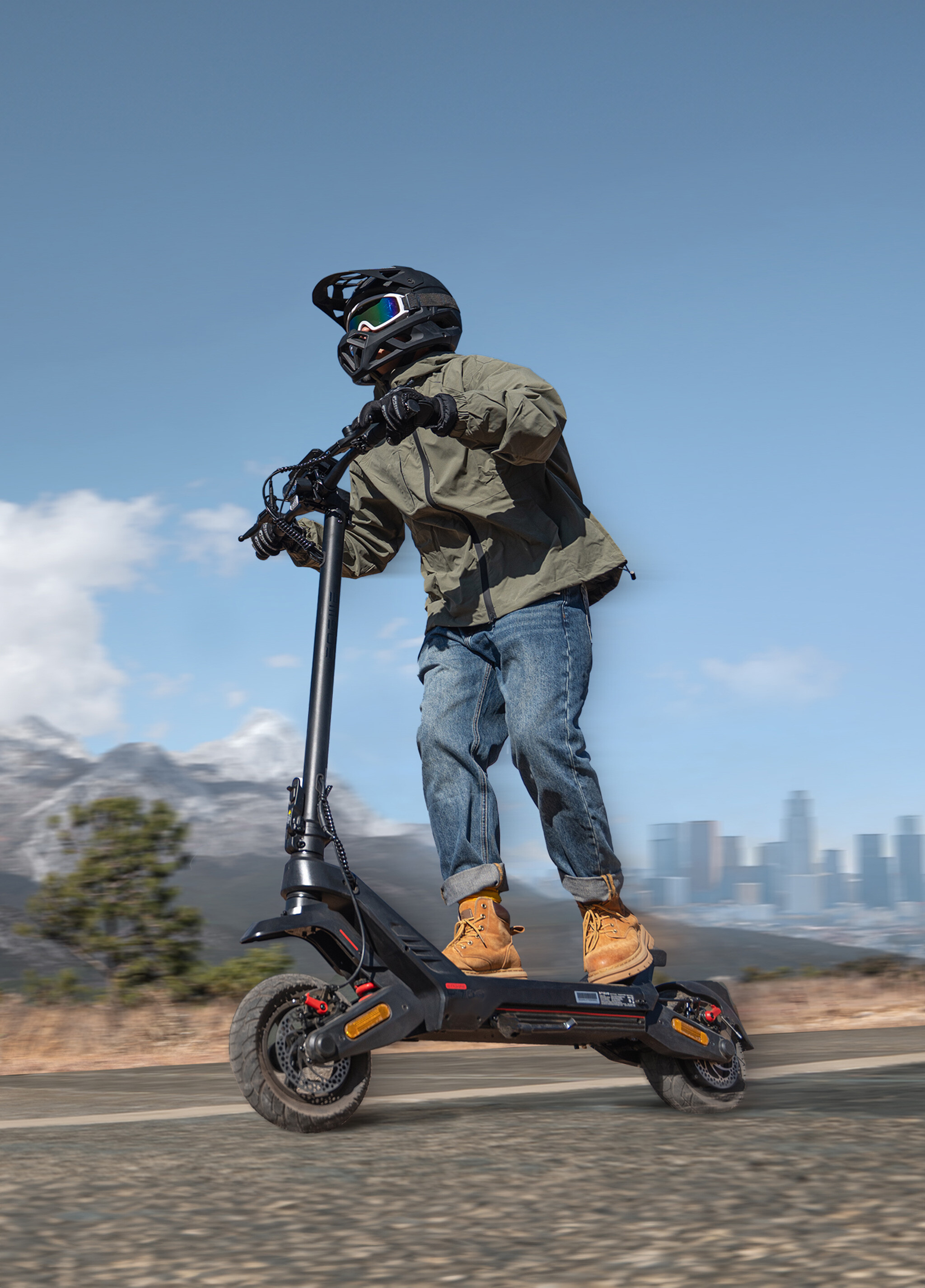 Eine Person mit Helm und Schutzbrille fährt auf einem schwarzen E-Scooter vor einer Stadt- und Bergkulisse.