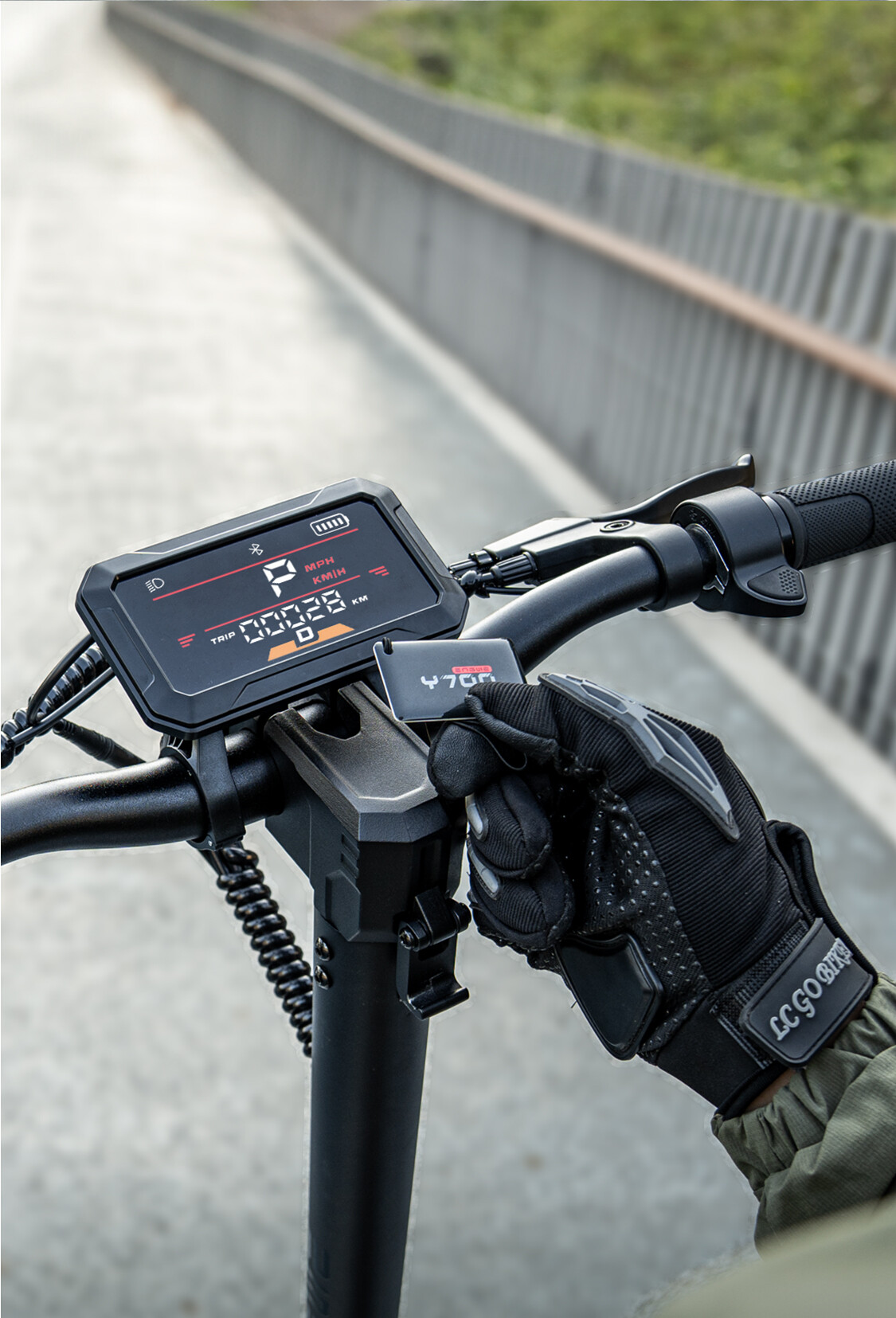 Ein schwarz-rotes Display am Lenker eines E-Scooters, ein behandschuhter Hand hält eine kleine Karte nah ran.