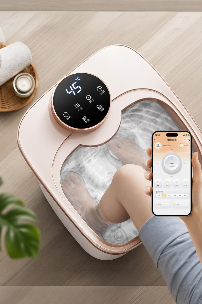 Bir kişi ahşap zemindeki pembe akıllı ayak masaj küvetini telefonla kontrol ediyor.