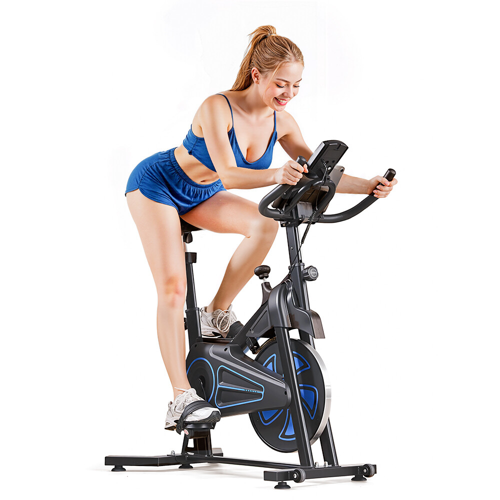 Una mujer sonriente con ropa deportiva azul hace ejercicio en una bicicleta estática negra sobre fondo blanco.