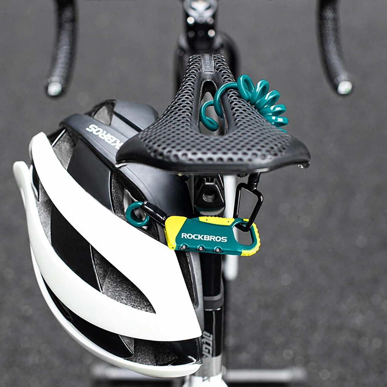 Ein weiß-schwarzer Fahrradhelm hängen am Sattel, gesichert mit einem grün-gelben Rockbros Kabelschloss.