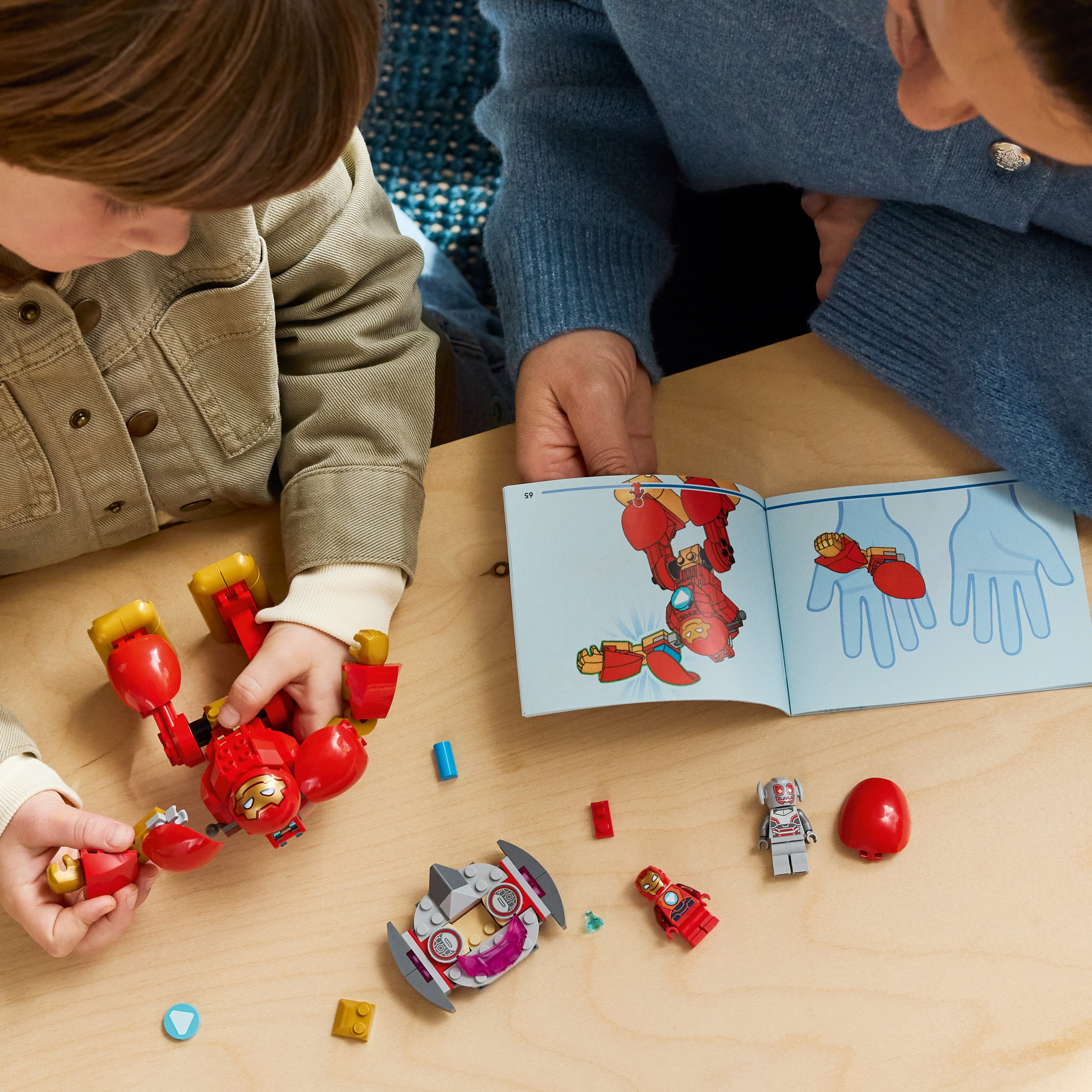Un niño y un adulto construyen figuras de Lego juntos en una mesa de madera.