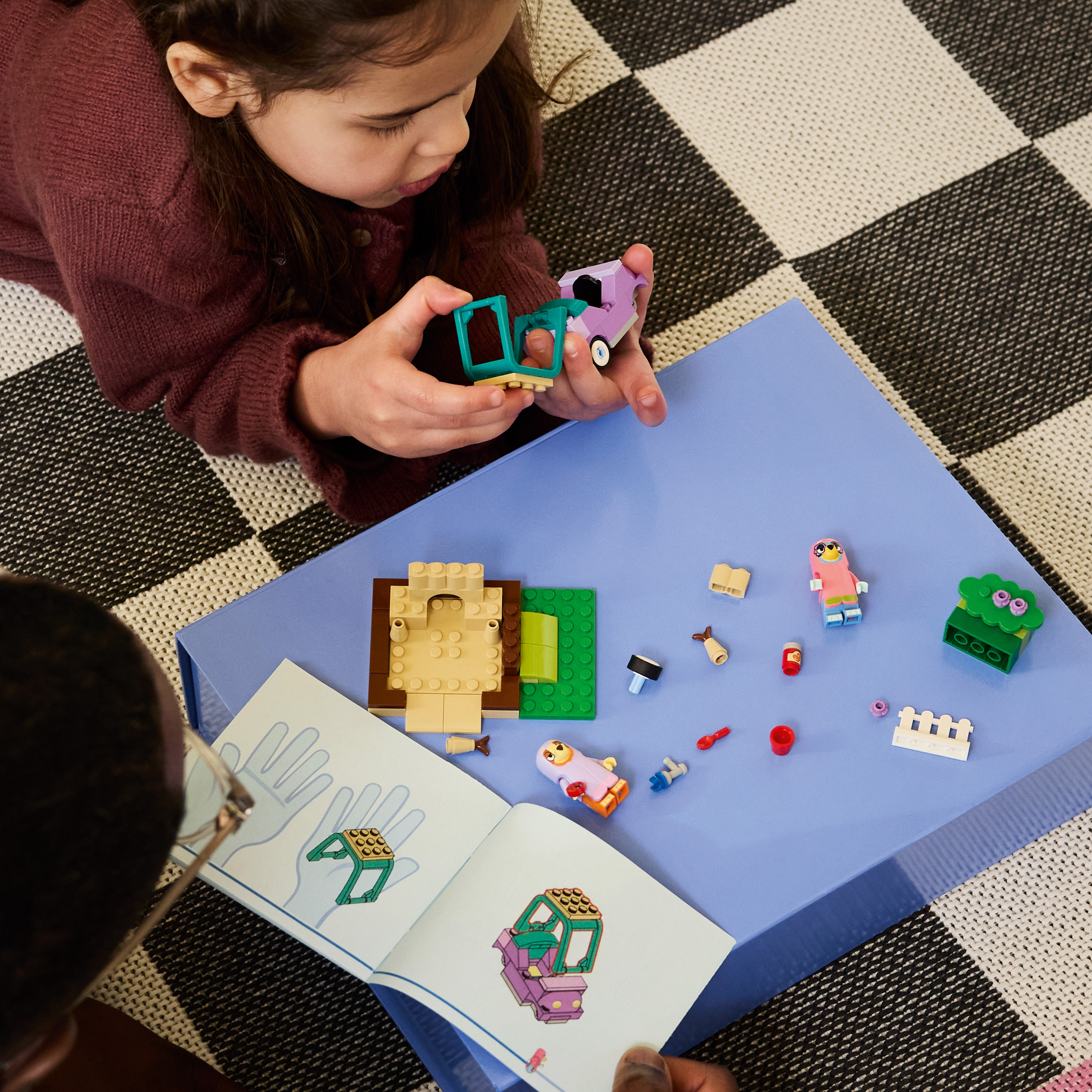 Una bambina che gioca con i blocchetti su una superficie blu, leggendo un manuale.
