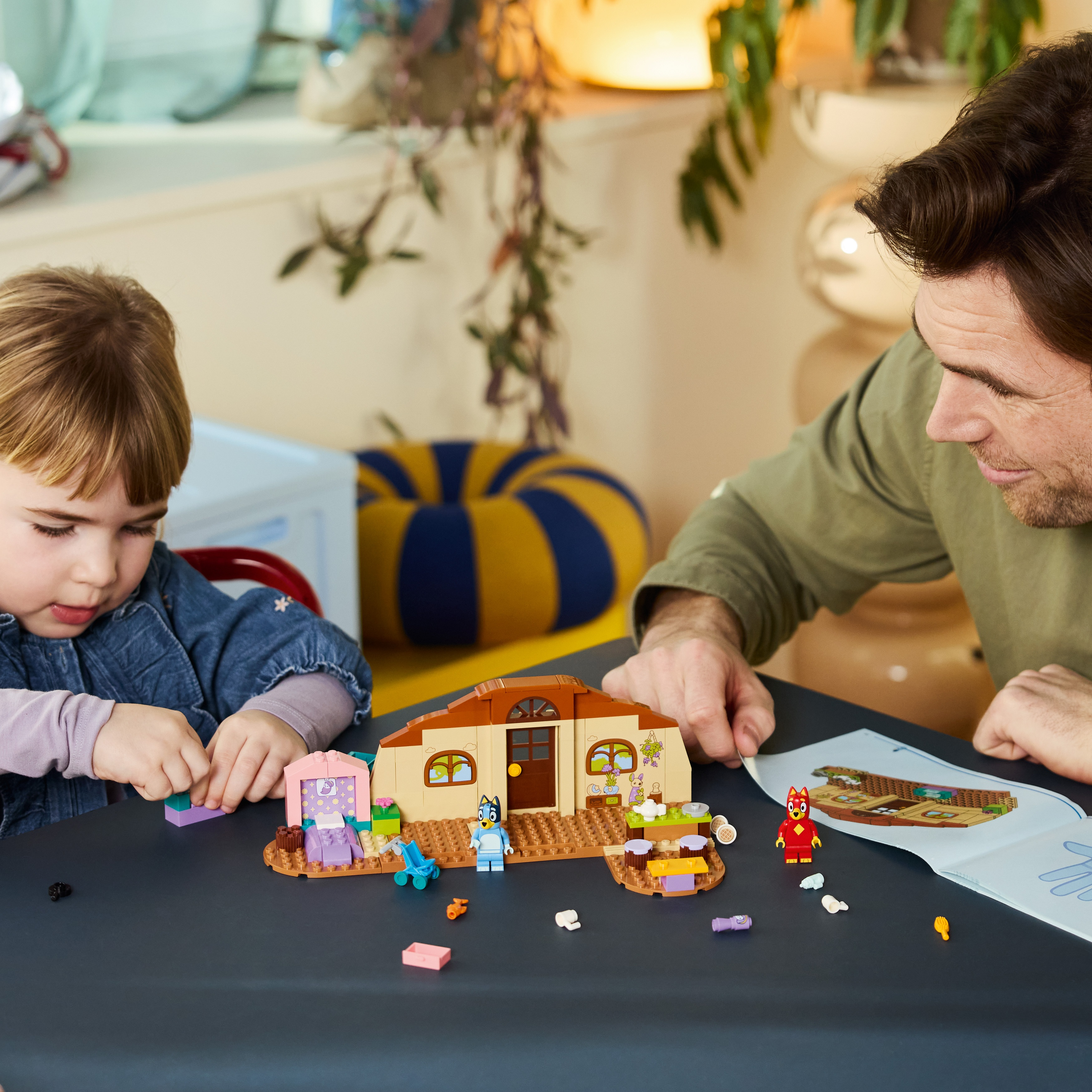 Un padre e la sua bambina siedono a un tavolo costruendo insieme una casa Lego.