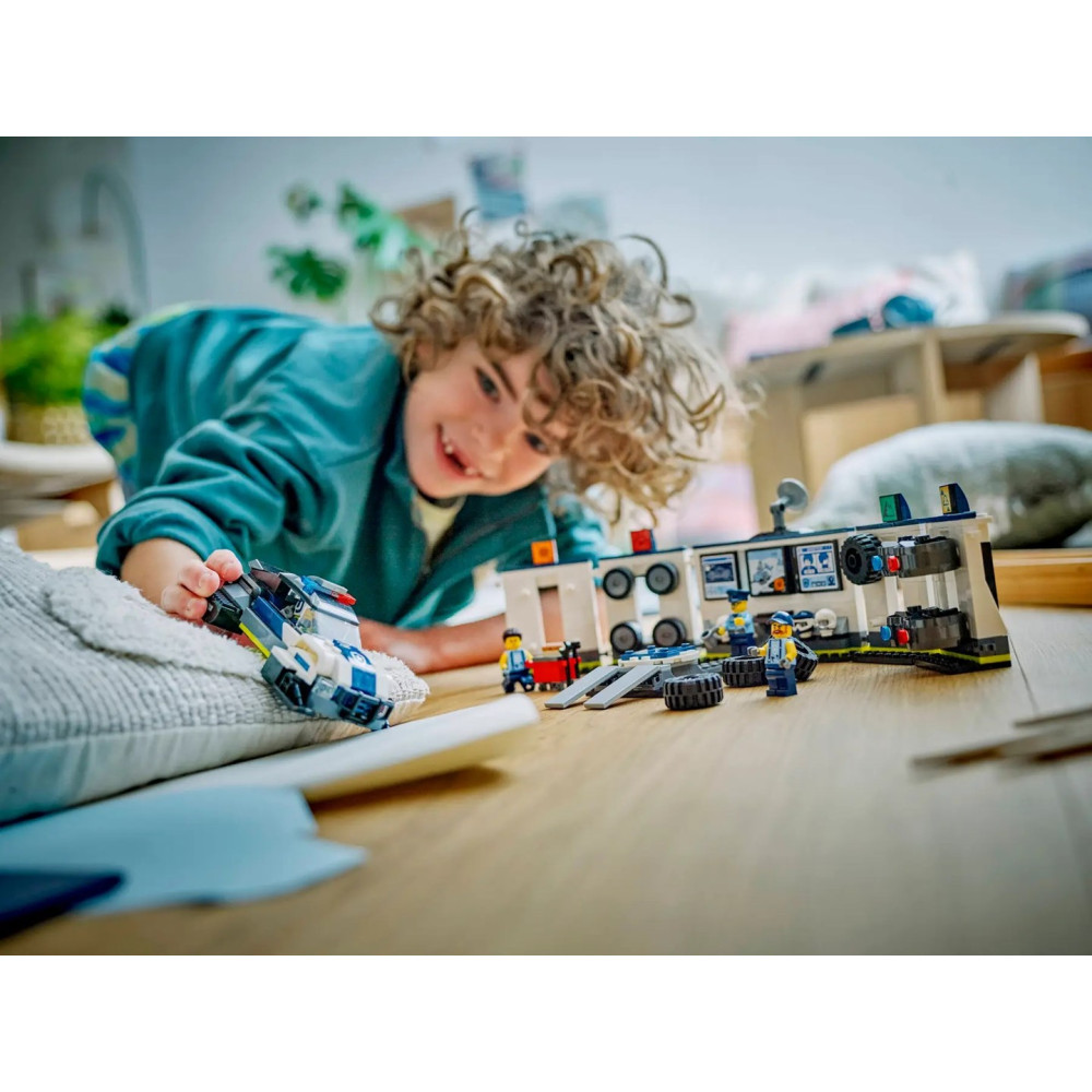 Kędzierzawy chłopak bawi się na drewnianej podłodze policyjnym autem Lego i komisariatem.