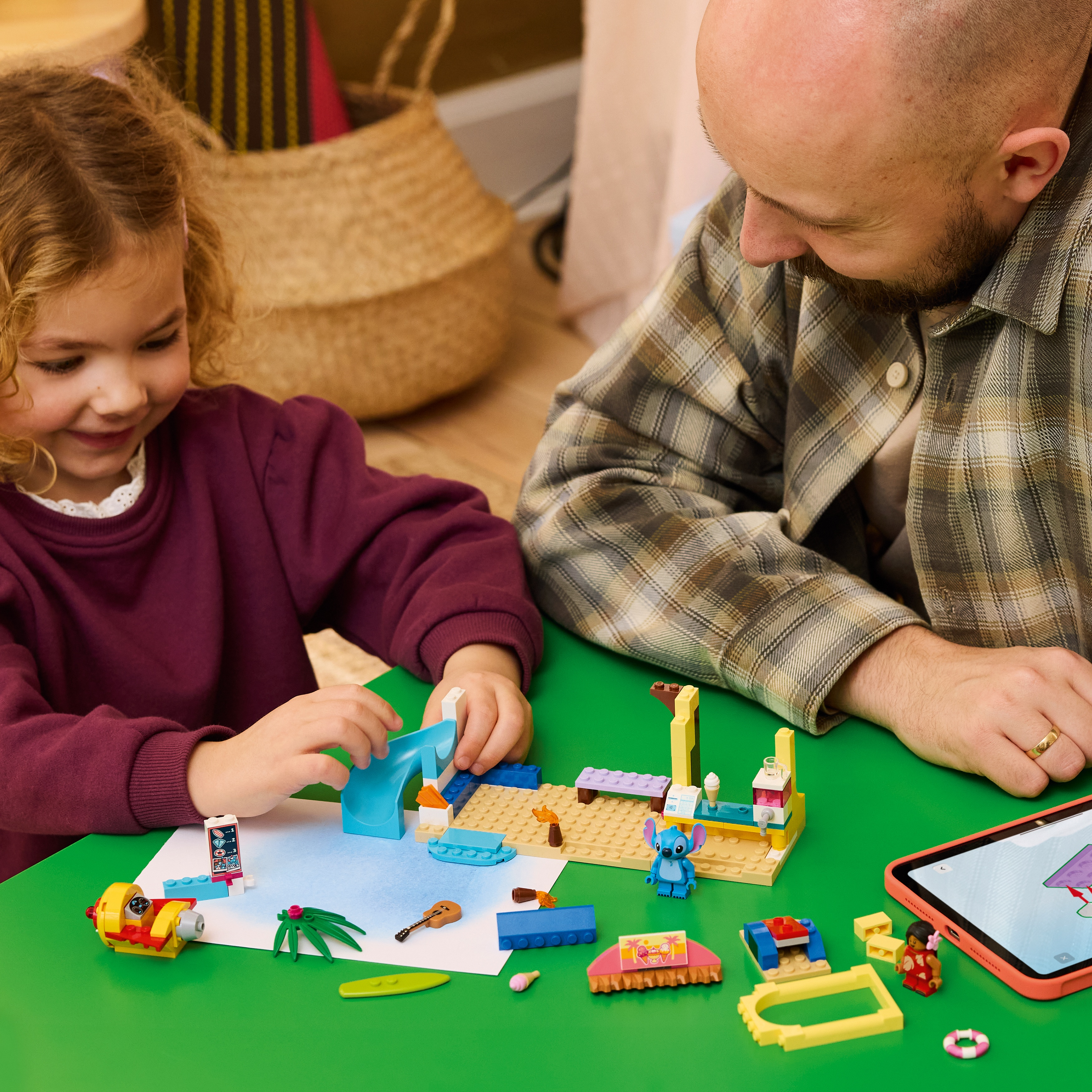 Una niña y su padre juegan con coloridos juguetes Lego en una mesa verde.