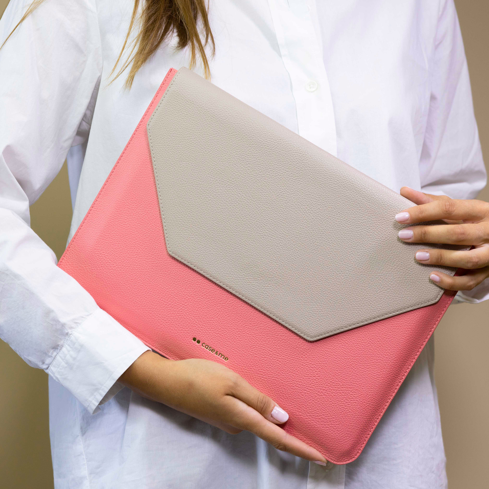 Una mujer con camisa blanca sostiene una funda para laptop rosa con solapa beige.
