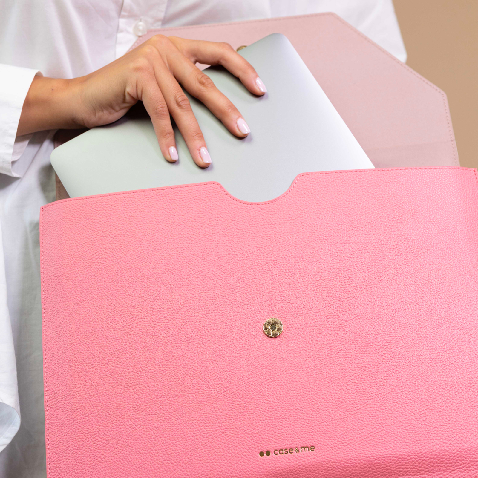 Una persona con camisa blanca guarda un portátil plateado en un estuche de cuero rosa con botón dorado.