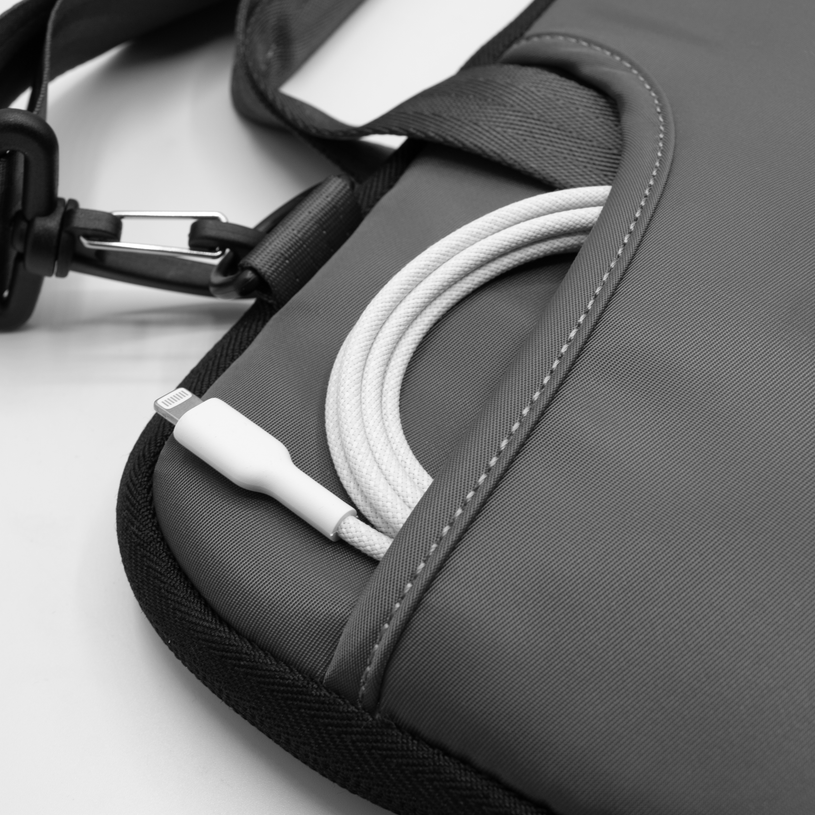 Un cable de carga blanco está enrollado en el bolsillo de una funda de portátil oscura.