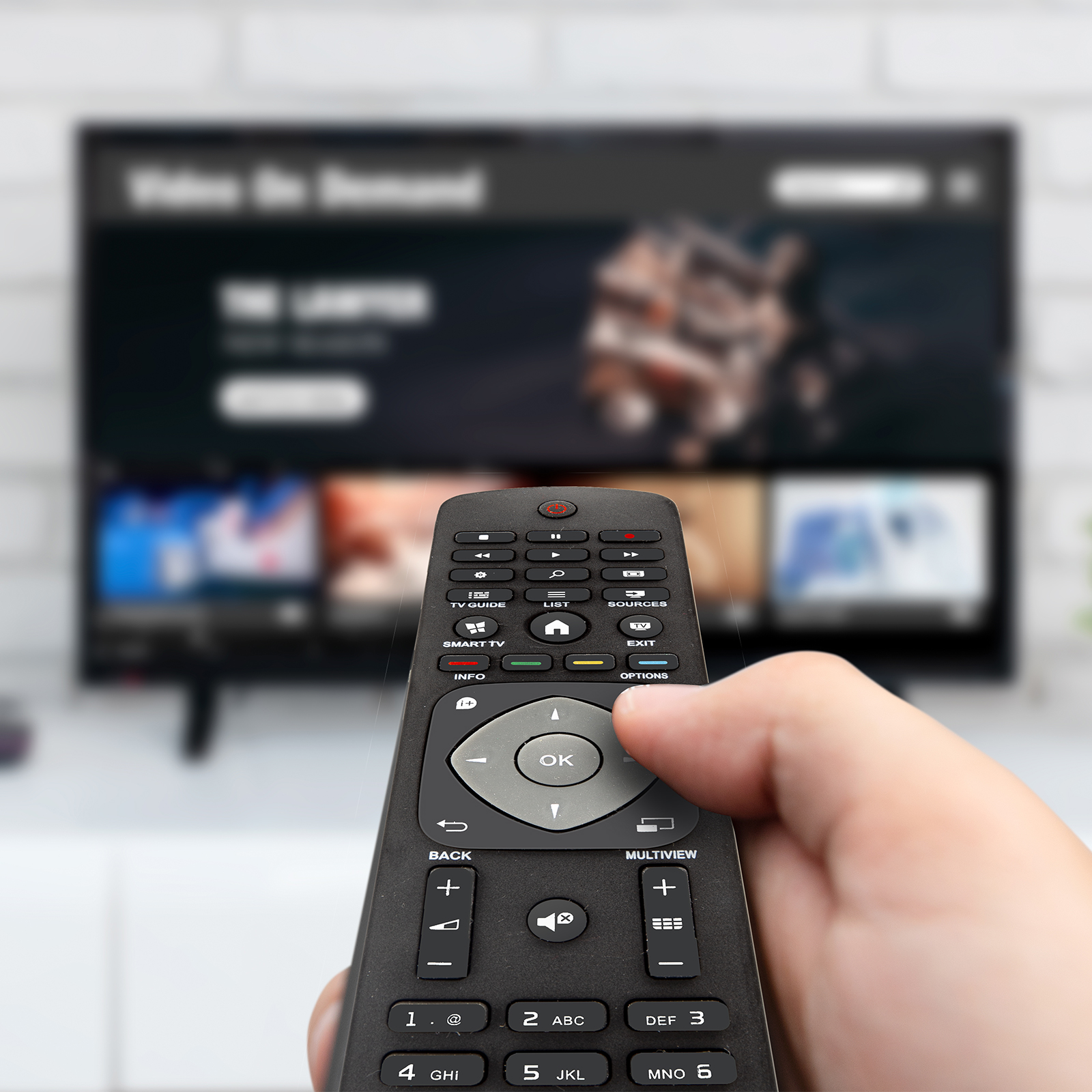 Mano che tiene un telecomando nero davanti a una televisione sfocata.