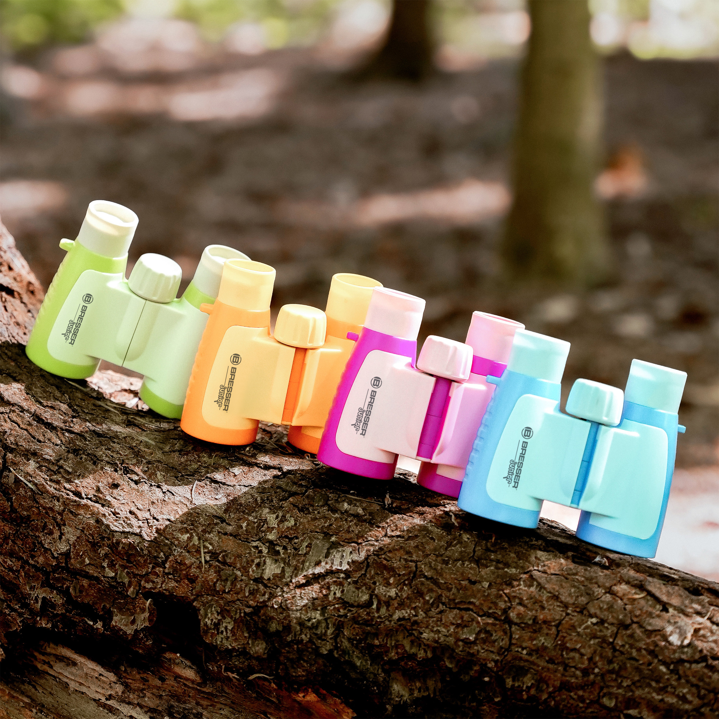 Eine Reihe bunter Kinderfernrohre liegt auf einem Baumstamm im Wald.