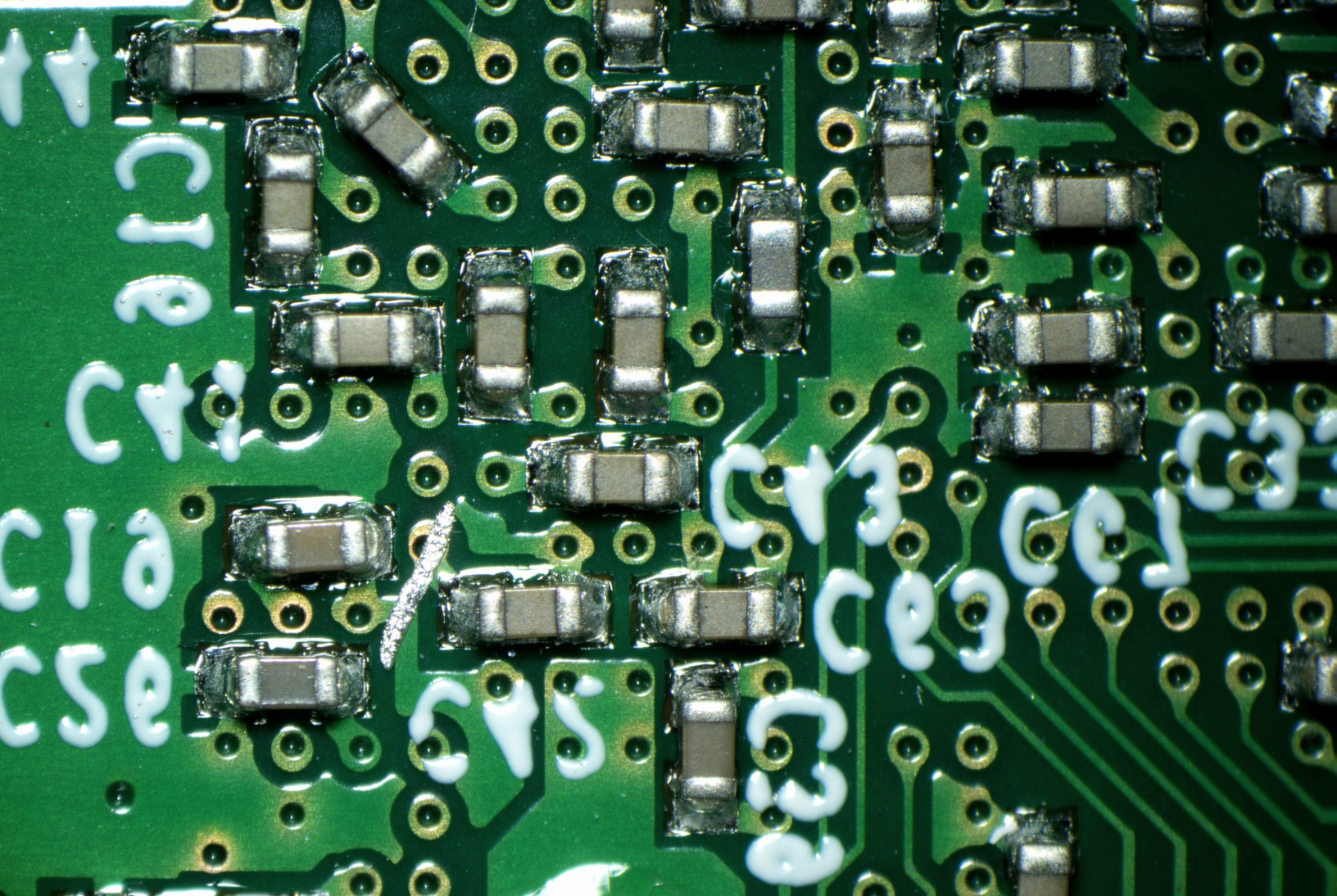 Nahaufnahme einer grünen Leiterplatte mit vielen kleinen elektronischen Bauteilen und weißer Beschriftung.
