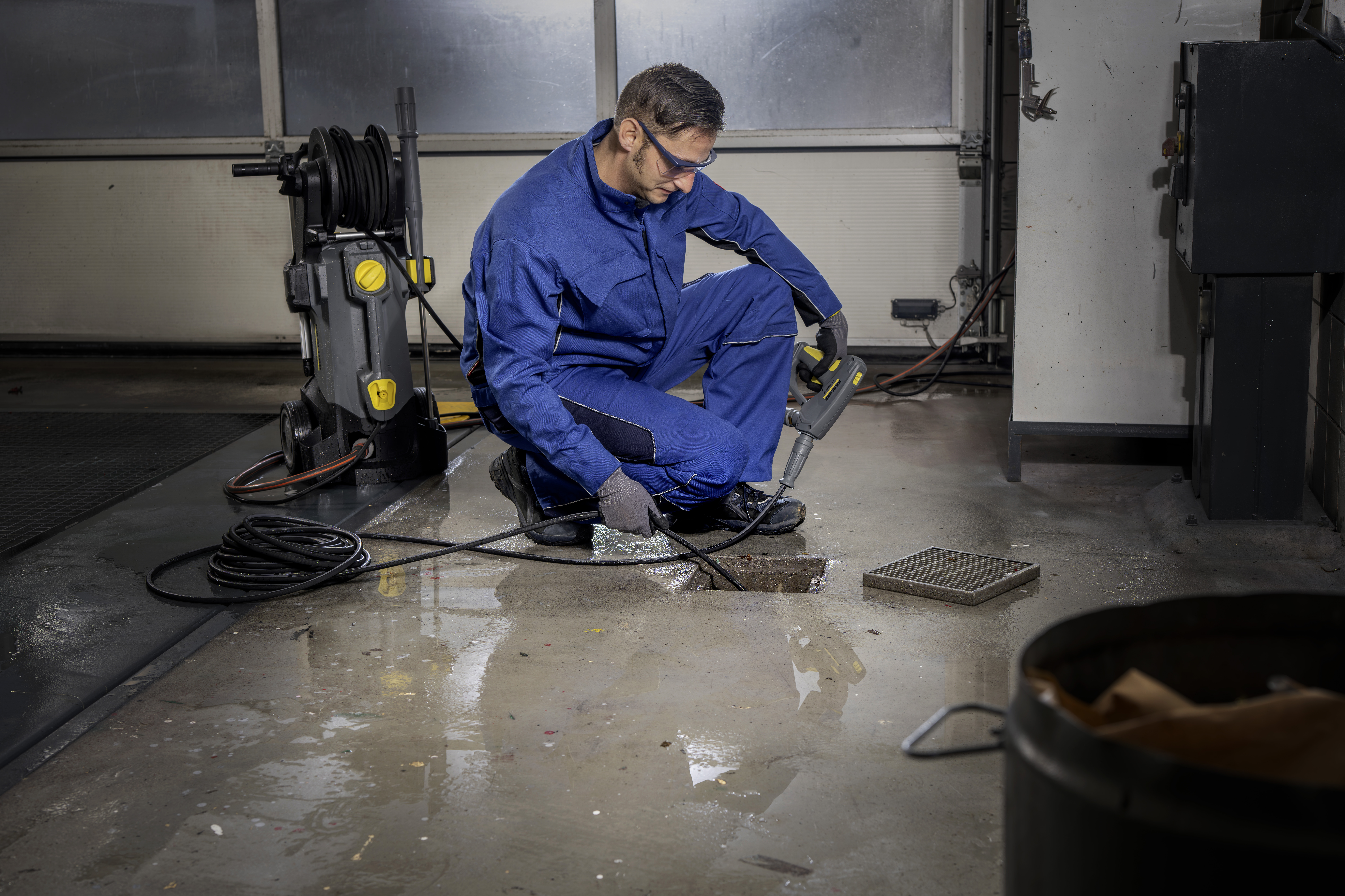 Ein Arbeiter in blauer Arbeitskleidung und Schutzbrille reinigt den Boden mit einem Hochdruckreiniger.