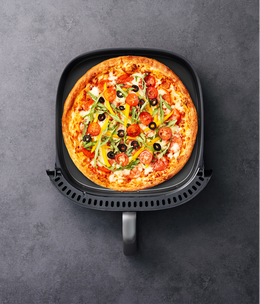 Eine Pizza mit Käse, Tomaten, Oliven und Kräutern in einem Heißluftfritteusenkorb.