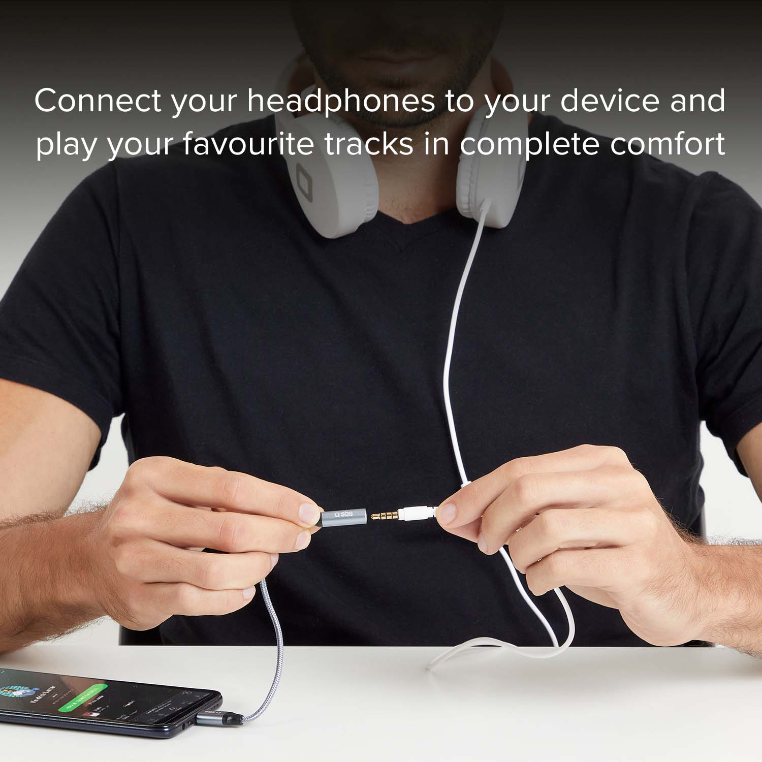 Un hombre con una camiseta negra conecta un cable de auriculares a un adaptador.